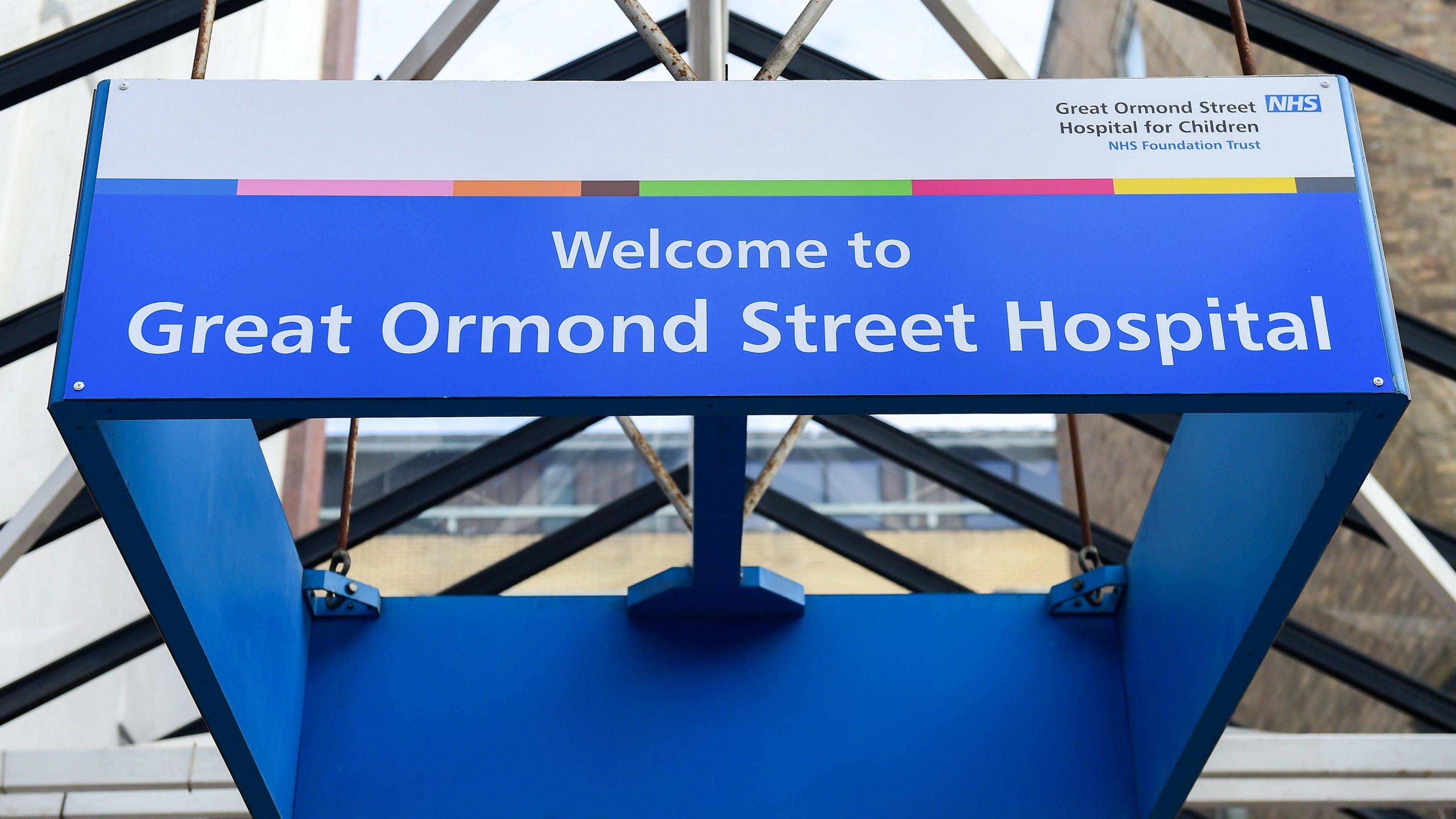 View looking up towards a glass roof with a suspended blue sign saying "Welcome to Great Ormond Street Hospital".