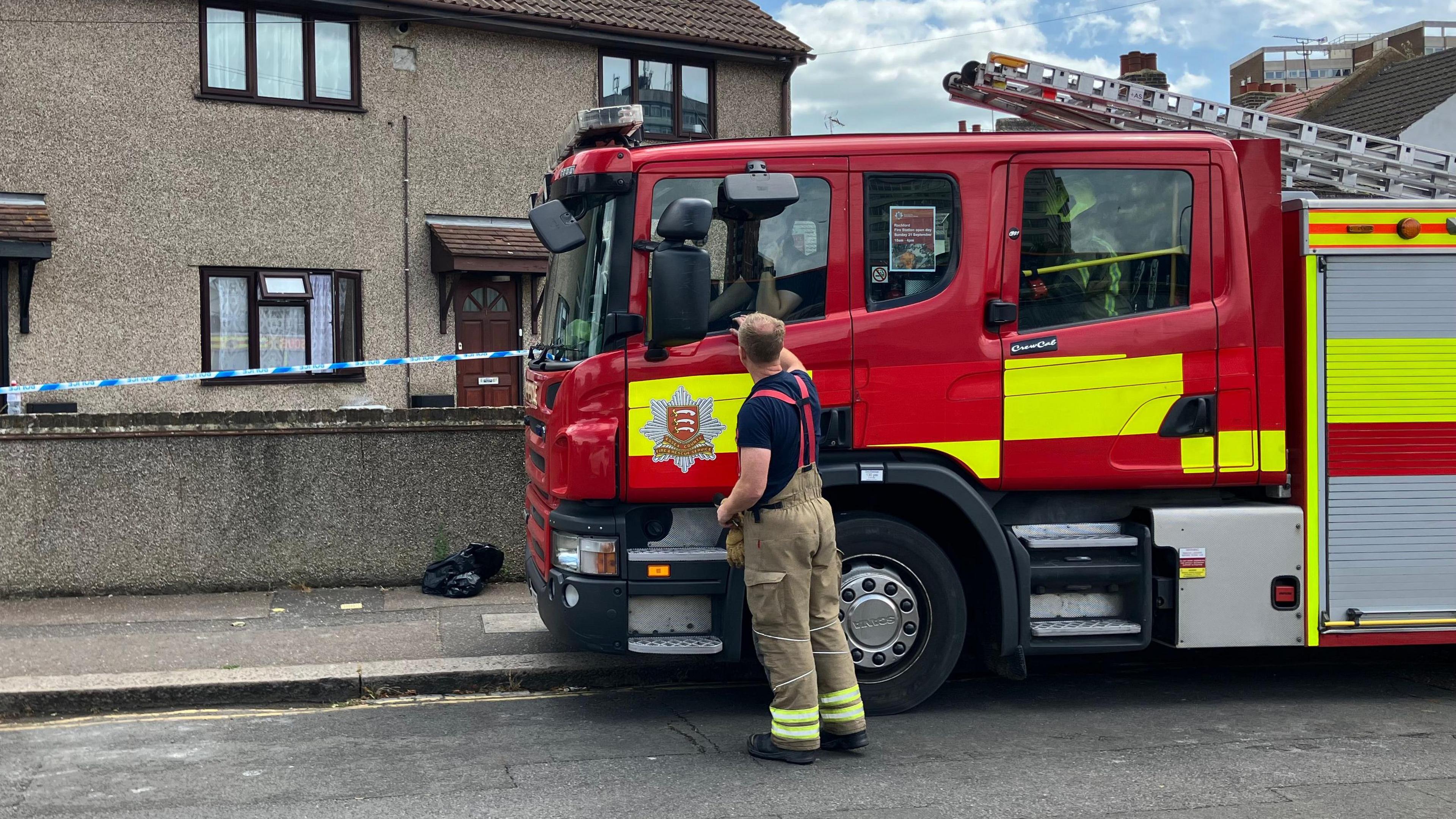 A red fire engine parked outside a house. There is also a police cordon in place.