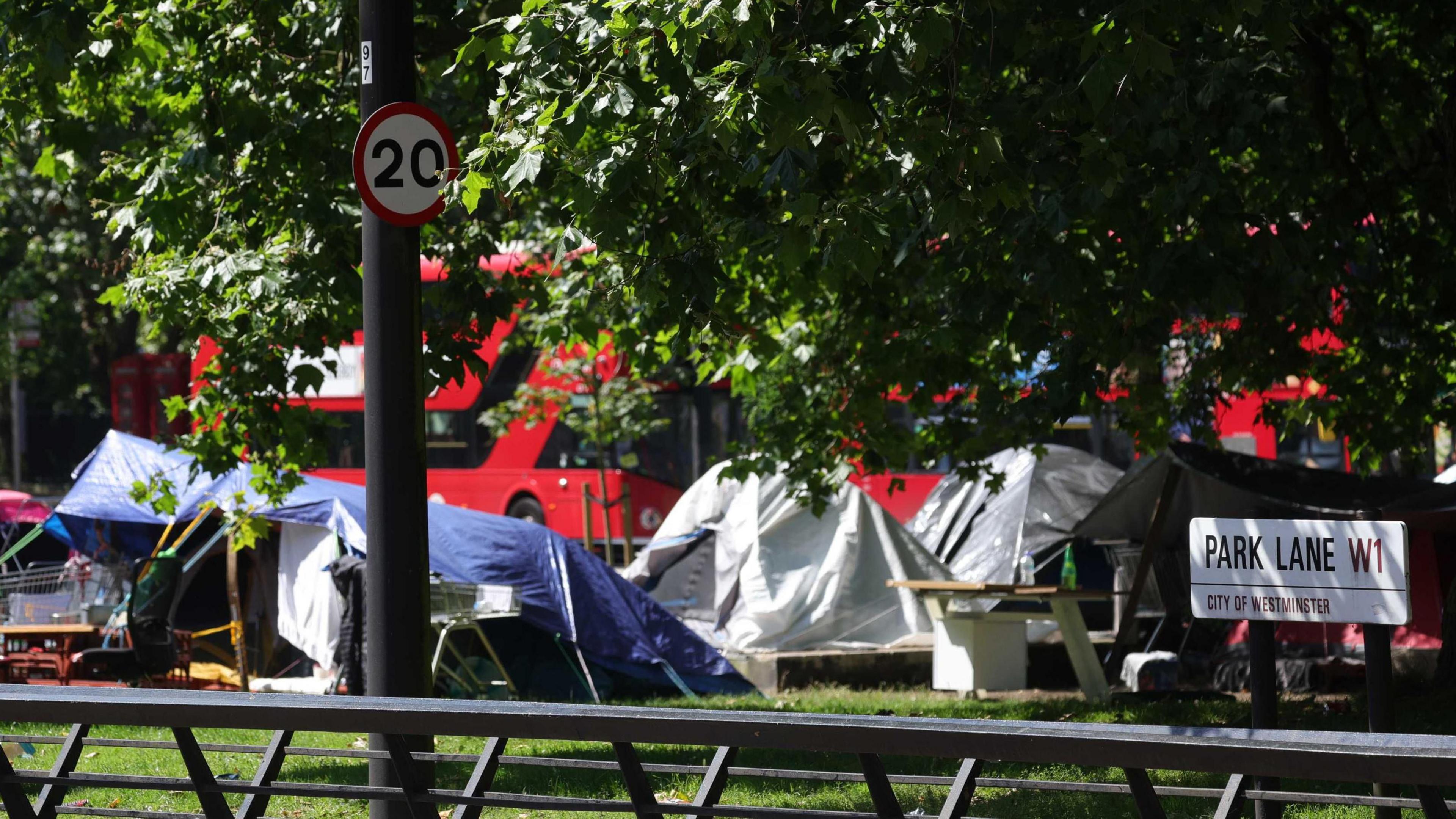 Tents pitched in a strip of land in Park Lane with London buses in the background. 