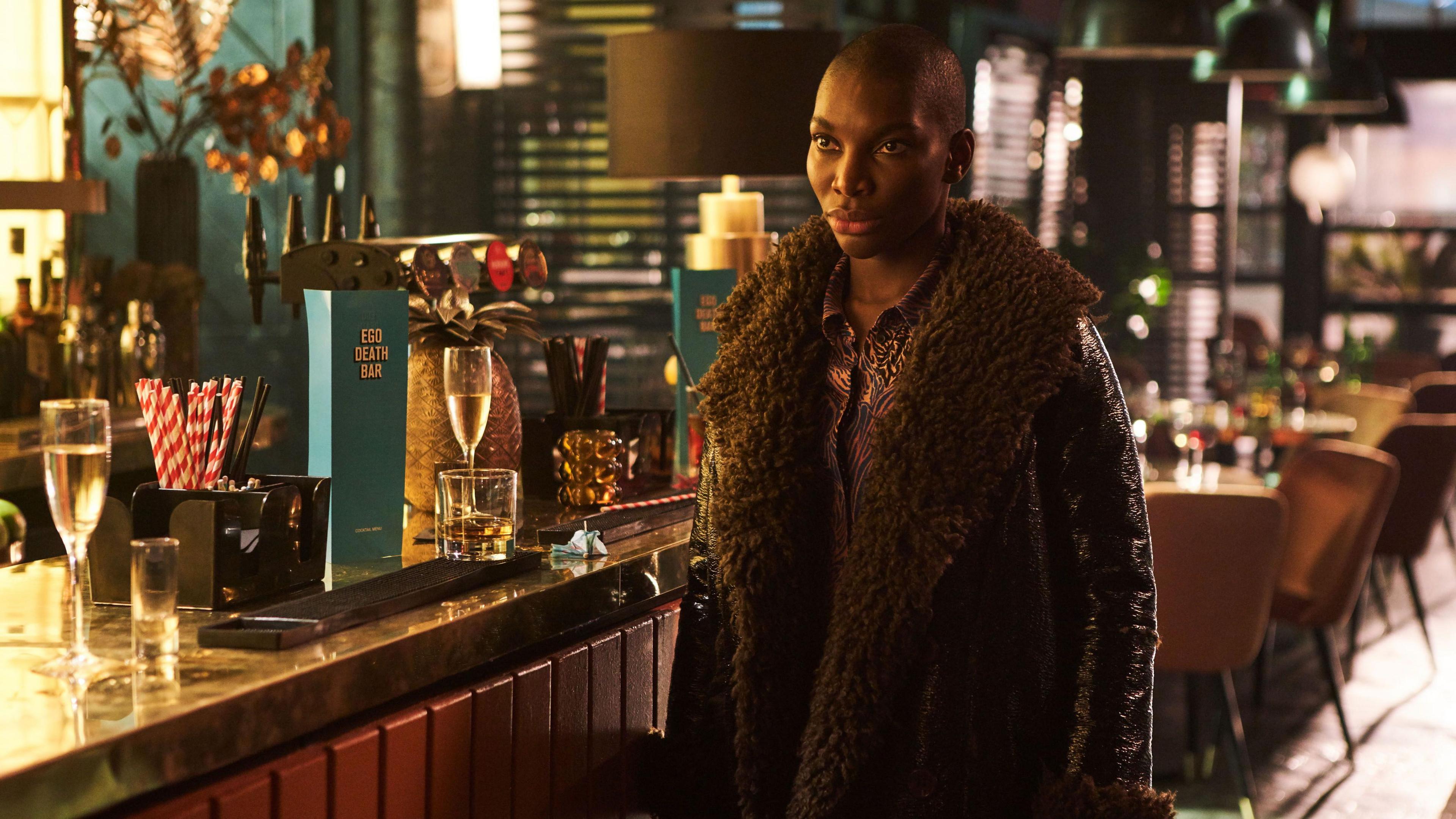 Michaela Coel's character Arabella wearing a fur and leather jacket at a bar