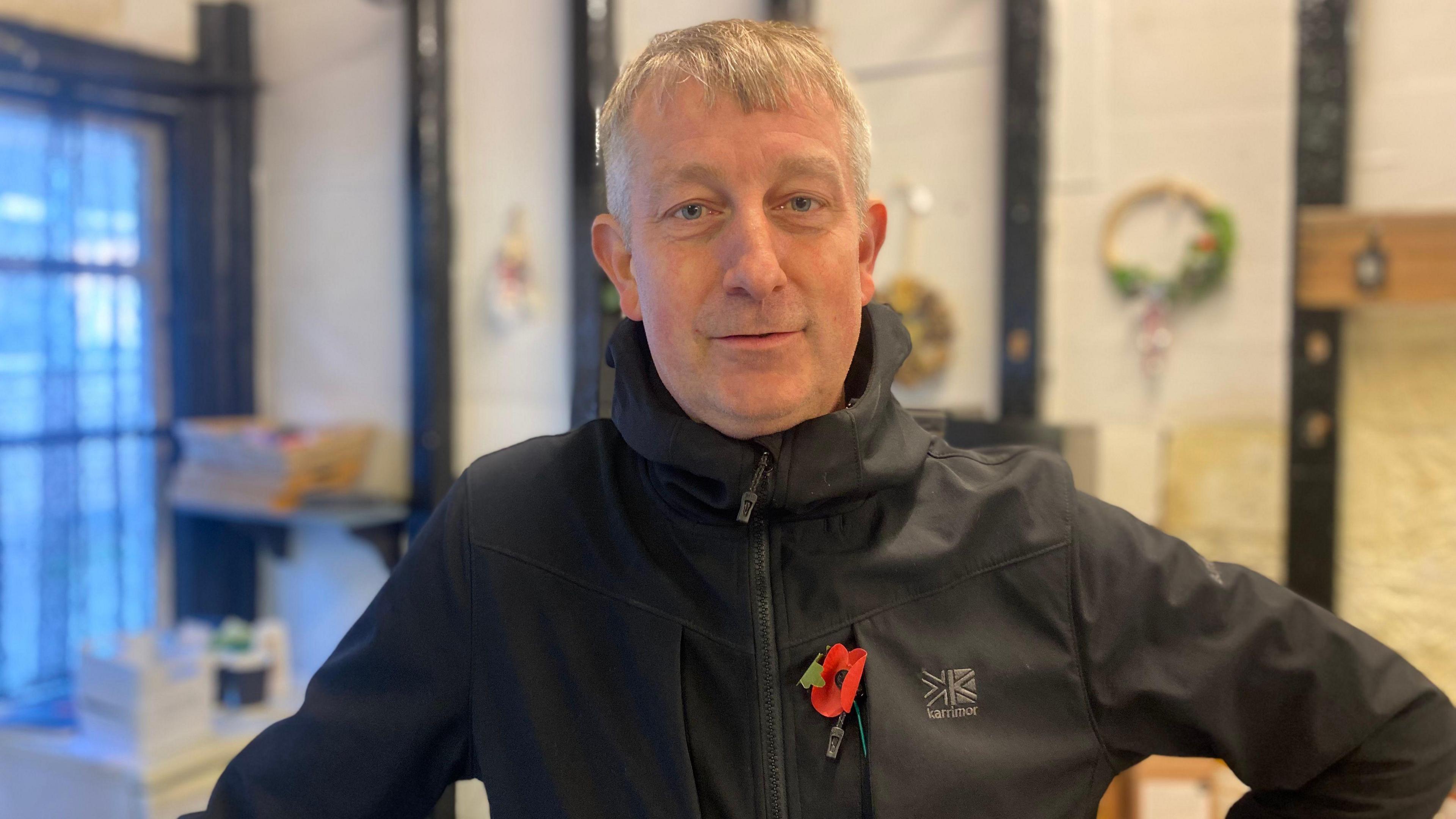 An image of a man with fair hair, wearing a black waterproof coat