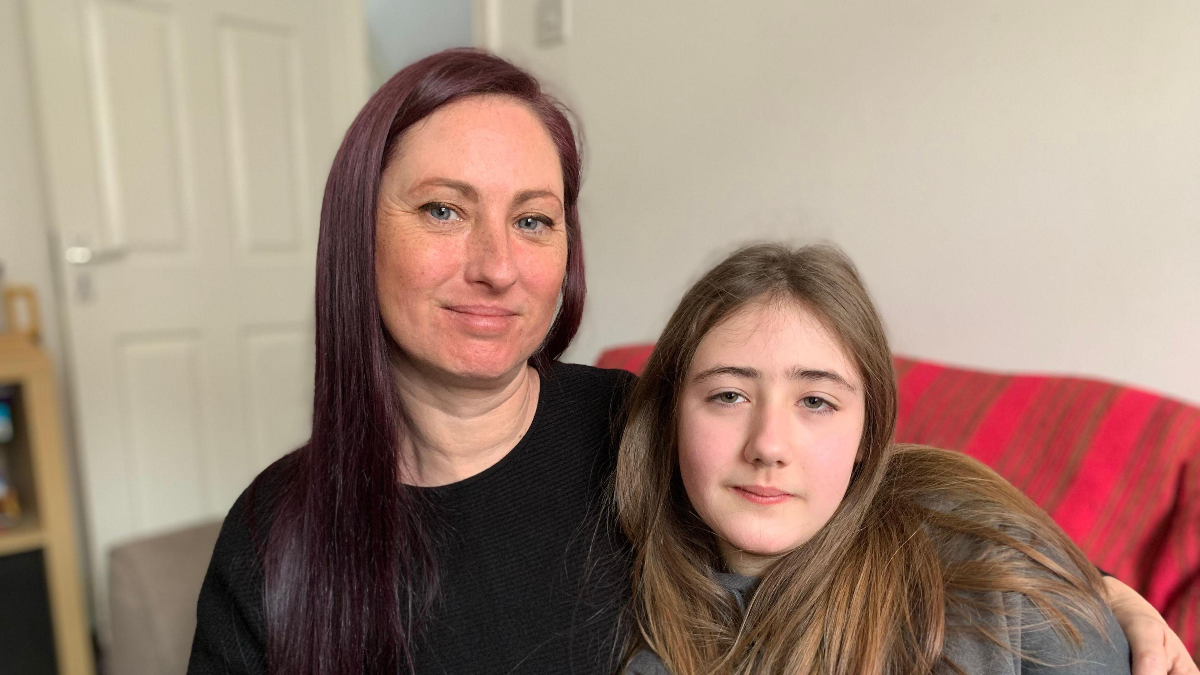 Emma and Lily-Rae, pictured from left to right, are sat on a sofa. Emma has her left arm wrapped around Lily-Rae and they are both smiling at the camera.