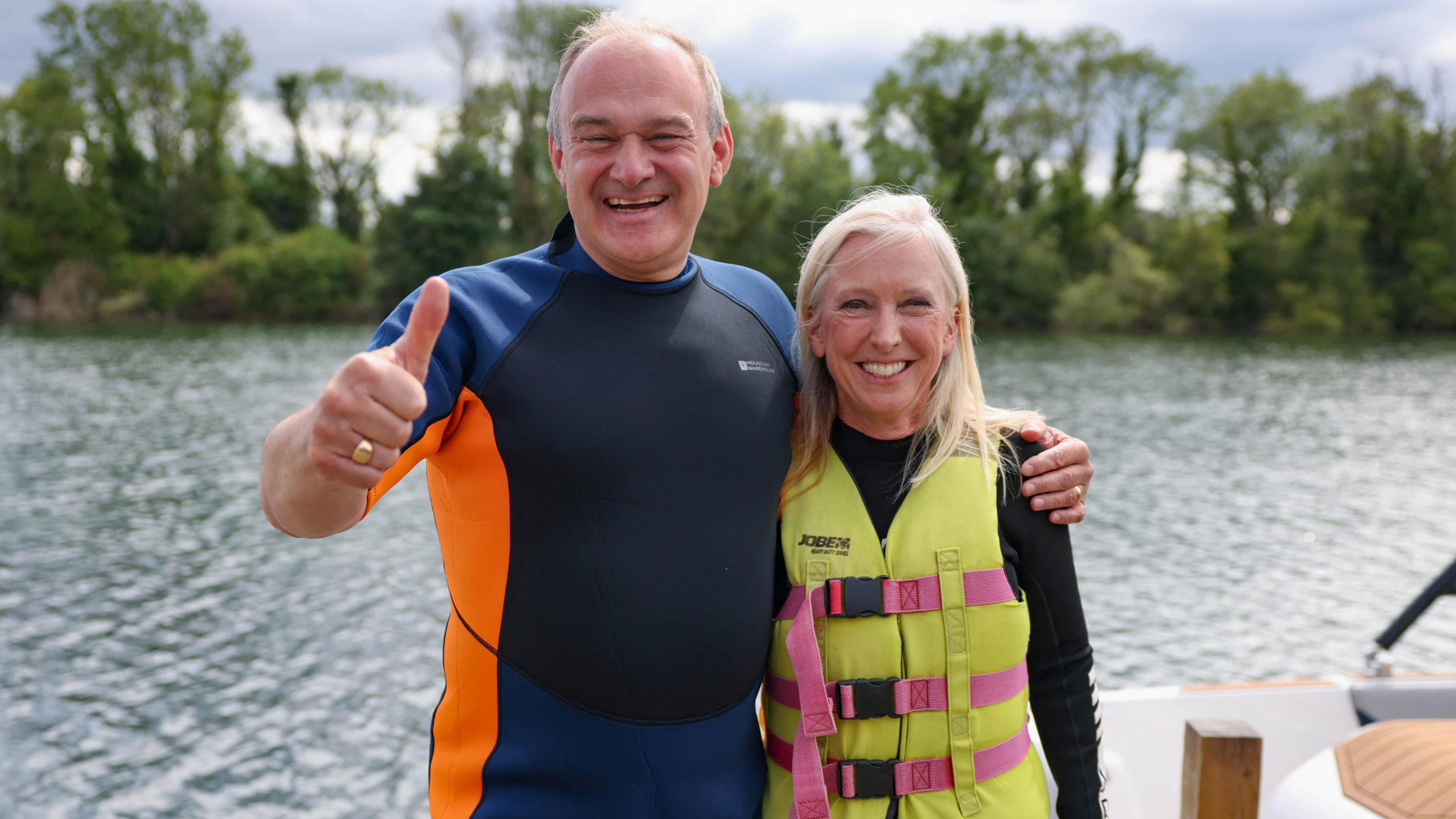 Dr Roz Savage wearing a life jacket with Sir Ed Davey wearing a wet suit in front of water 