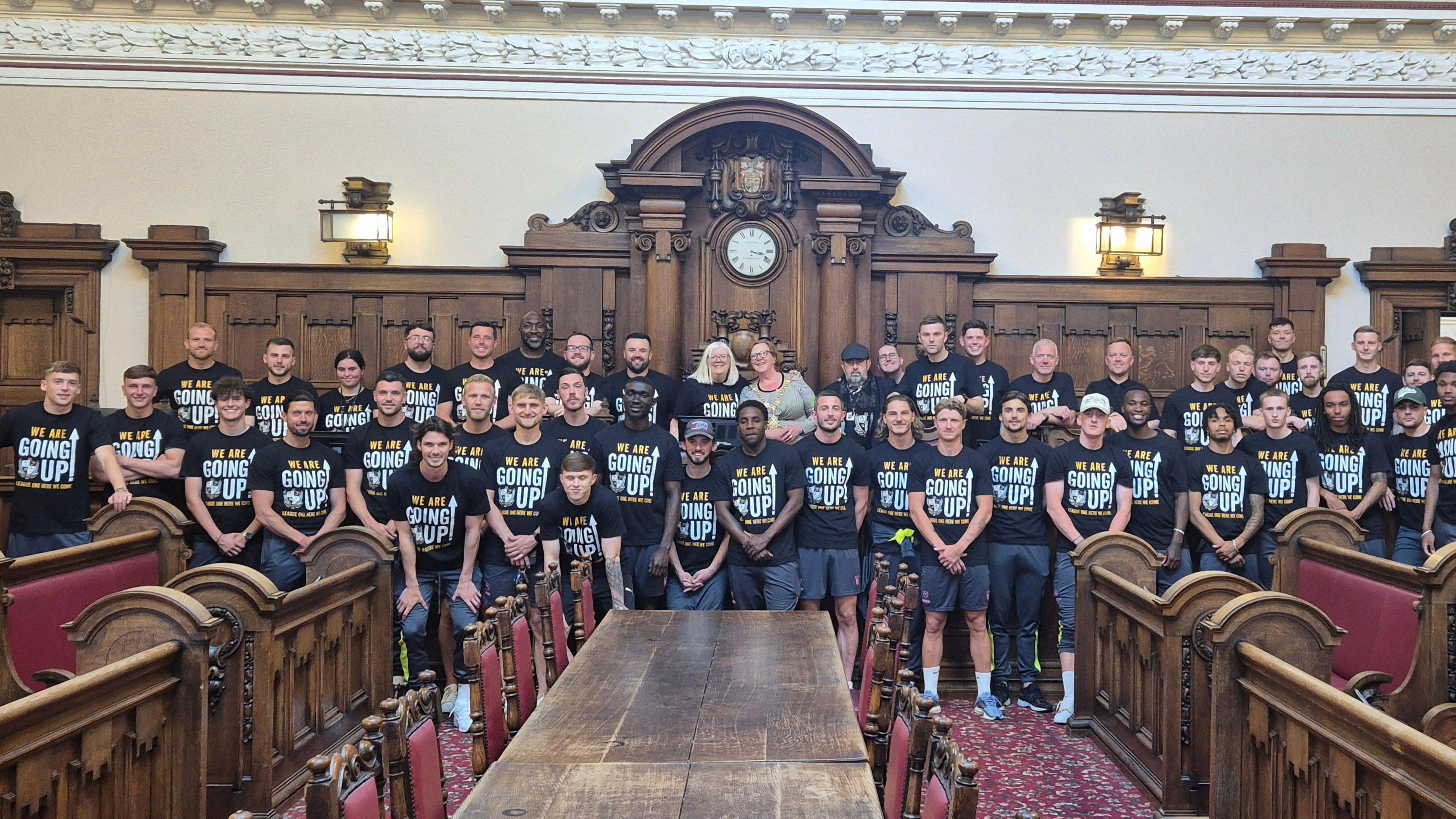 Port Vale at a civic reception with the Lord Mayor. The whole team is lined up wearing matching t-shirts. The Lord Mayor is at the back. They are in a grand civic building.