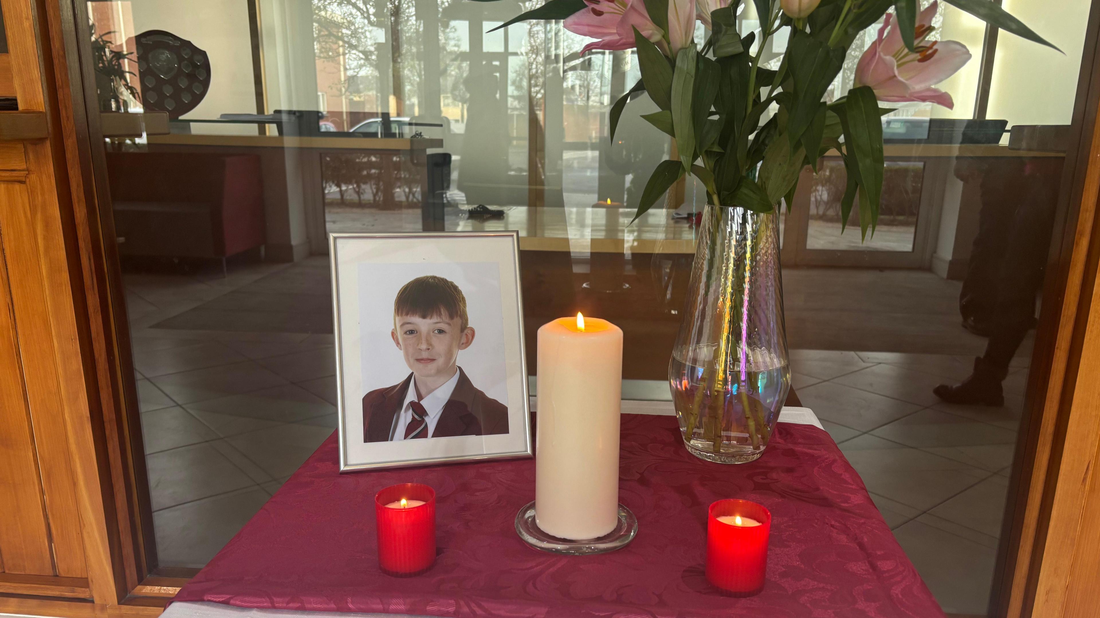 Several candles beside a framed photograph of Tiarnan Trainor, he is wearing a red school blazer and tie