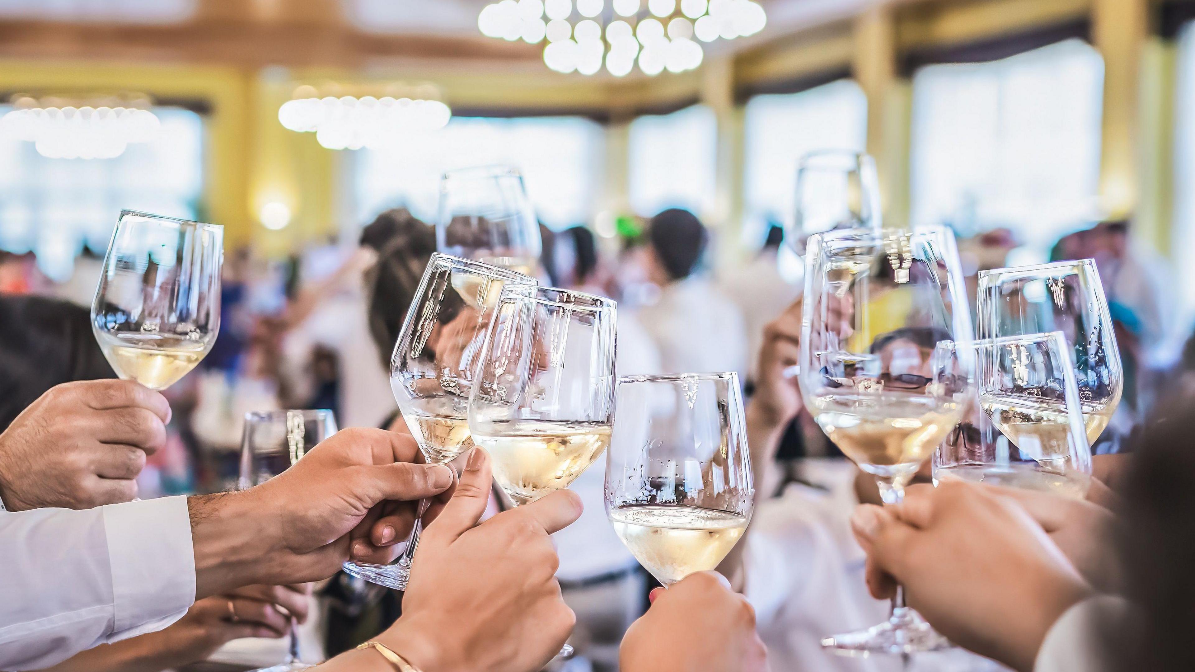 Several glasses filled with white wine being held aloft in a celebration