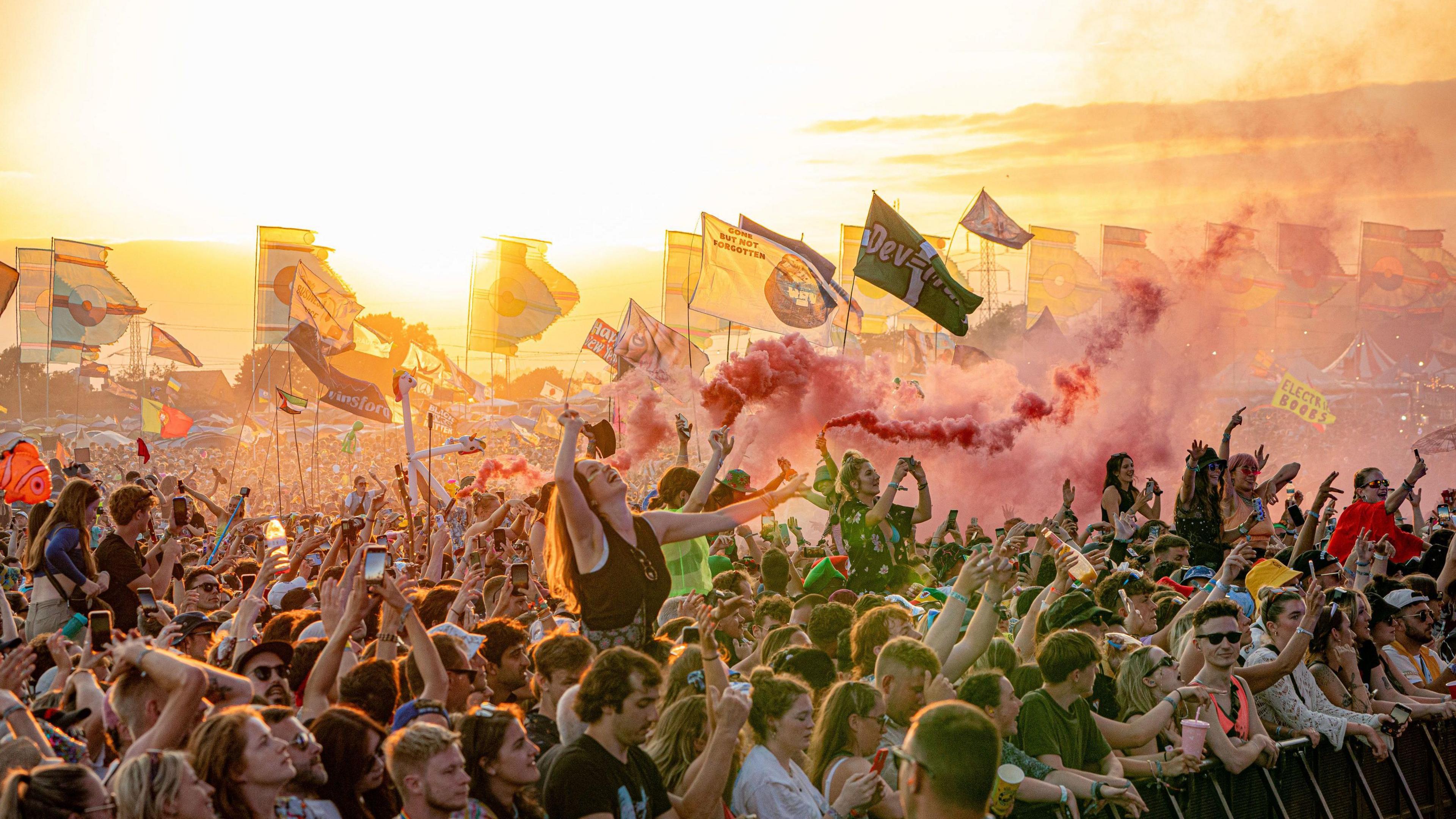 A large cloud waving flags at Glastonbury festival with a setting Sun behind