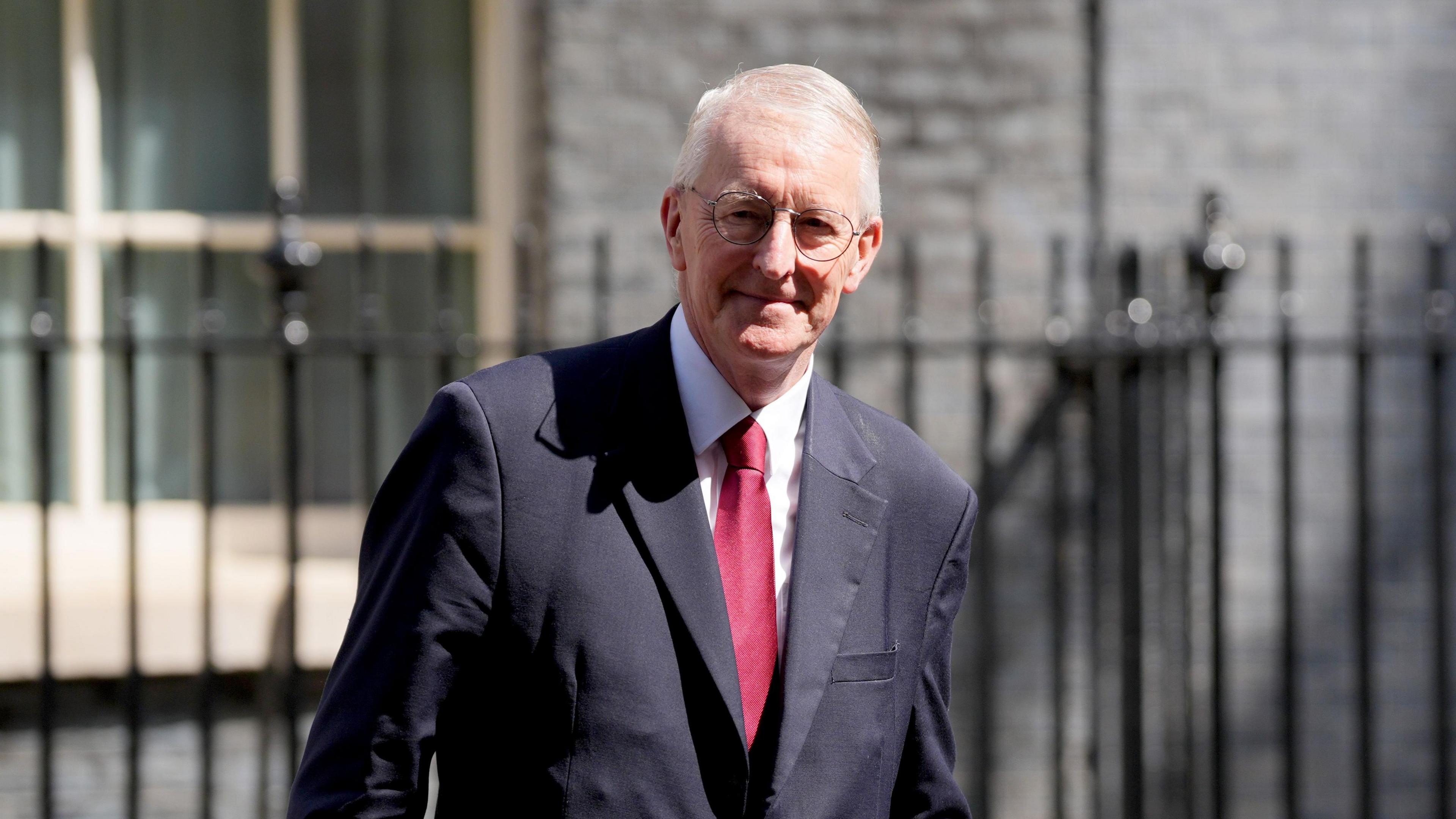 Hilary Benn outside 10 Downing Street. He has grey hair and glasses and is wearing a dark suit with a red tie.