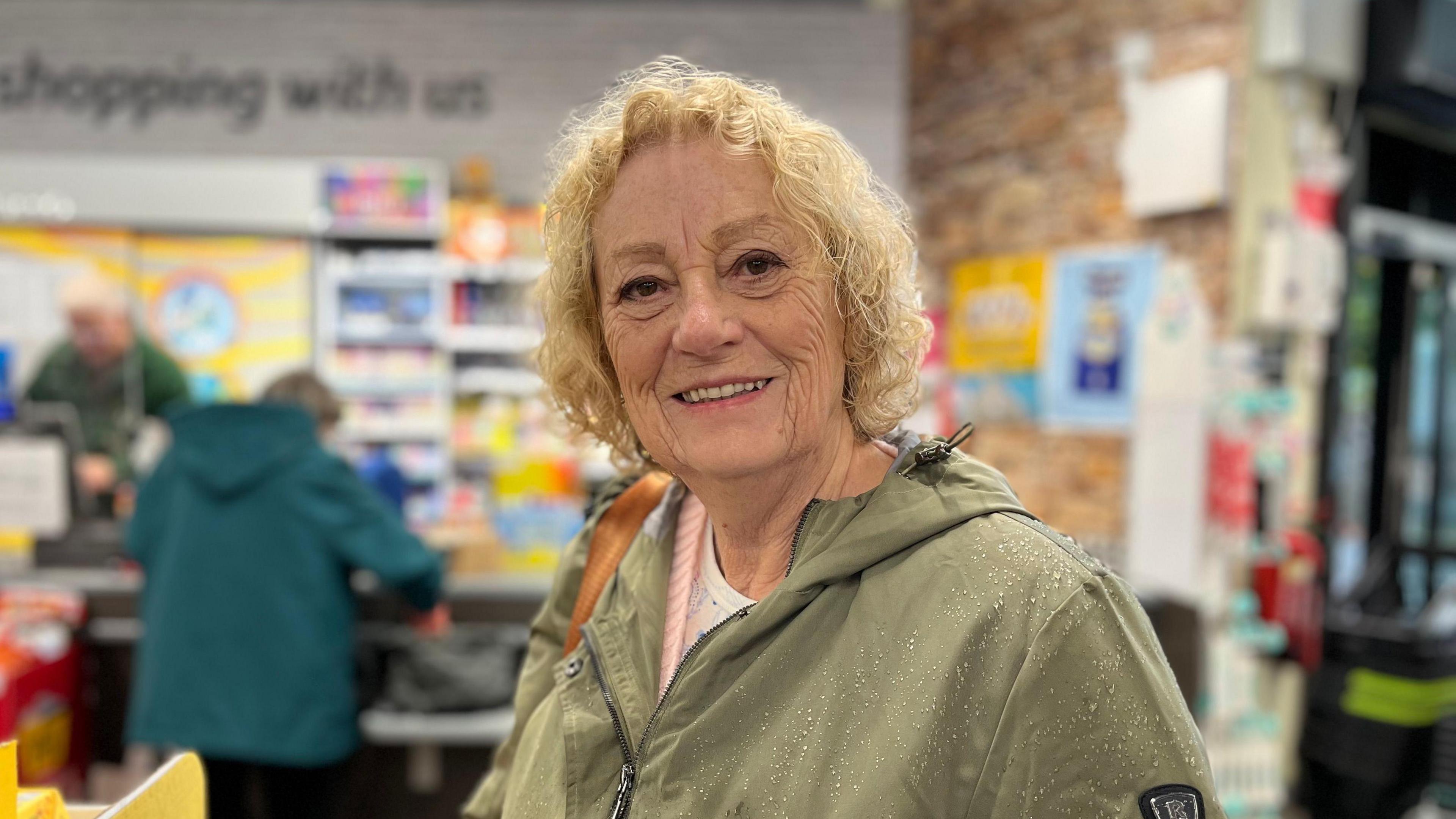 A woman wearing a green waterproof coat stands in a petrol station shop.