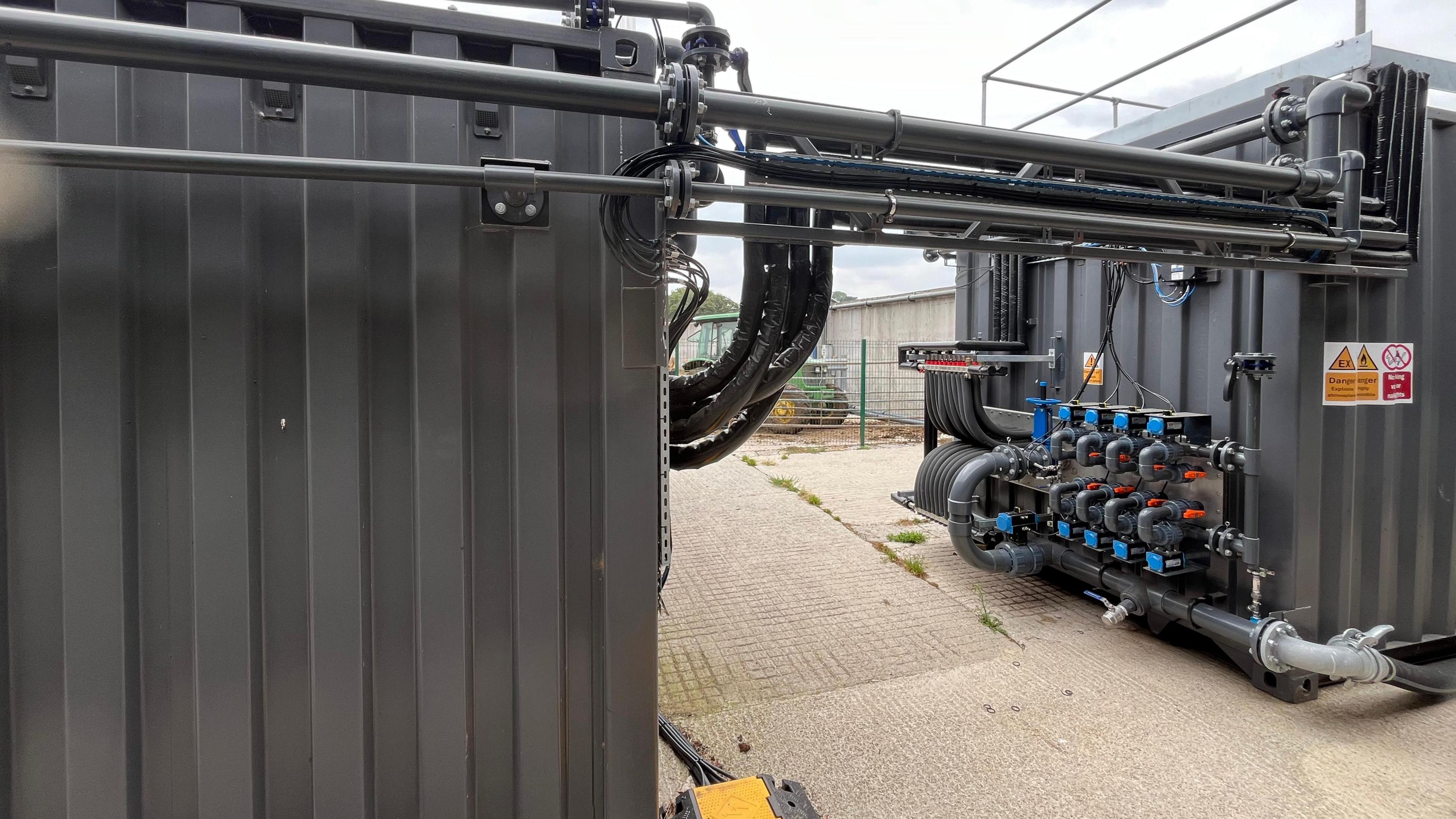 Two grey shipping containers next to each other - but they have been added too with lots of specialist piping.