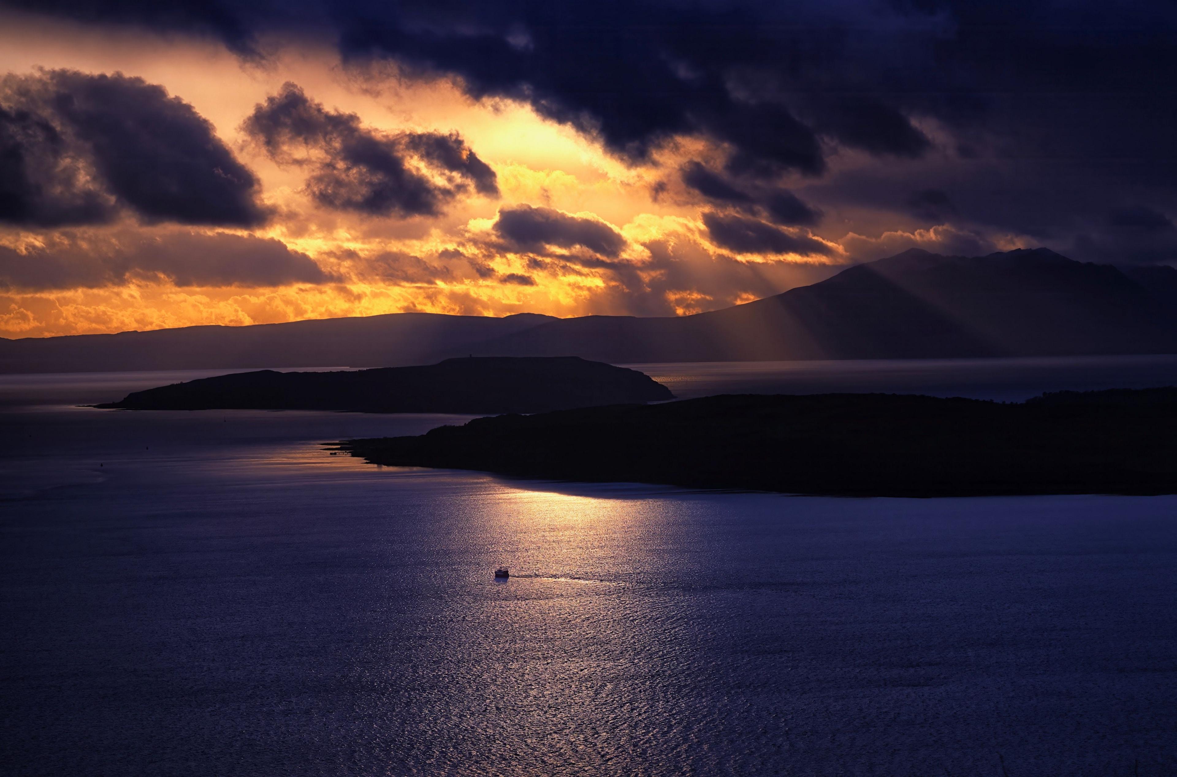 The outlines of two islands are just about visible in a striking sunset with orange-yellow light piercing through dark clouds