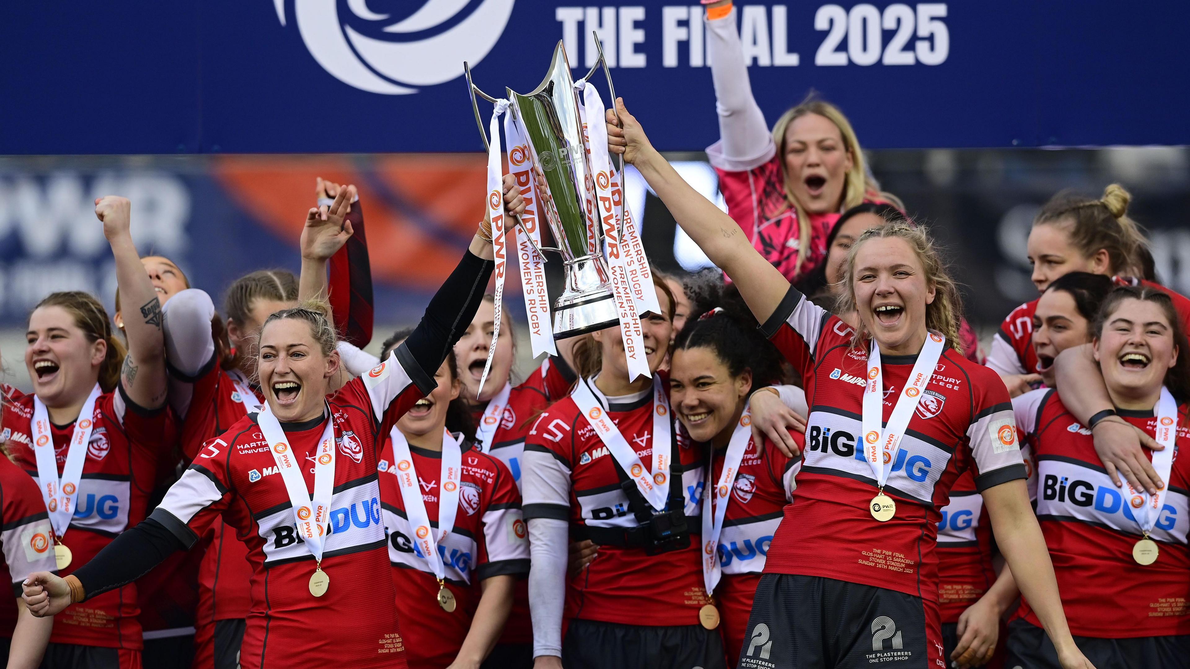 Gloucester-Hartpury captains Natasha 'Mo' Hunt (left) and Zoe Aldcroft (right) lift the PWR trophy with their team-mates behind them