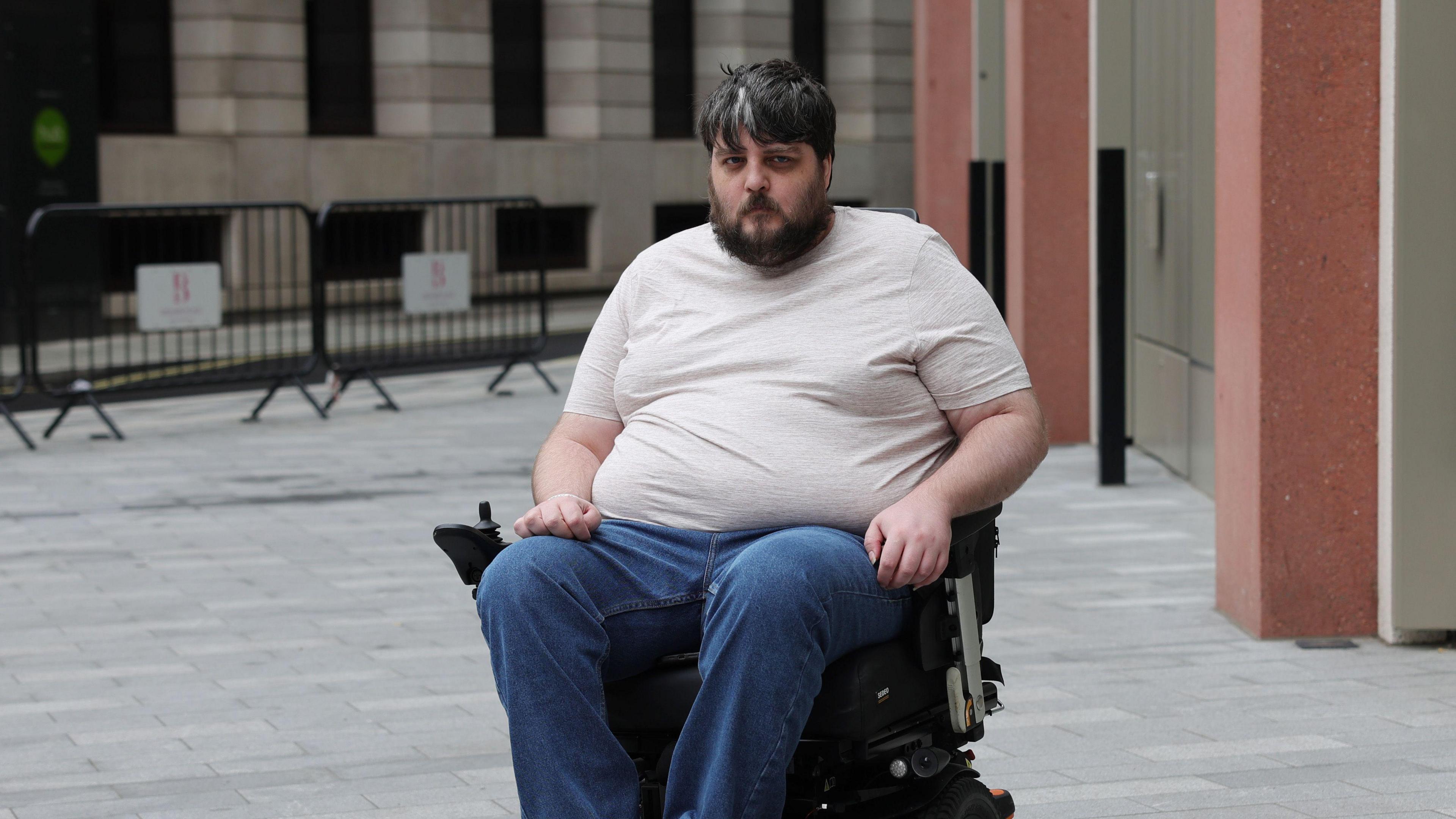 Nathan Rollinson, a man with brown and grey hair and a beard in a light t-shirt sitting in a black electric wheelchair