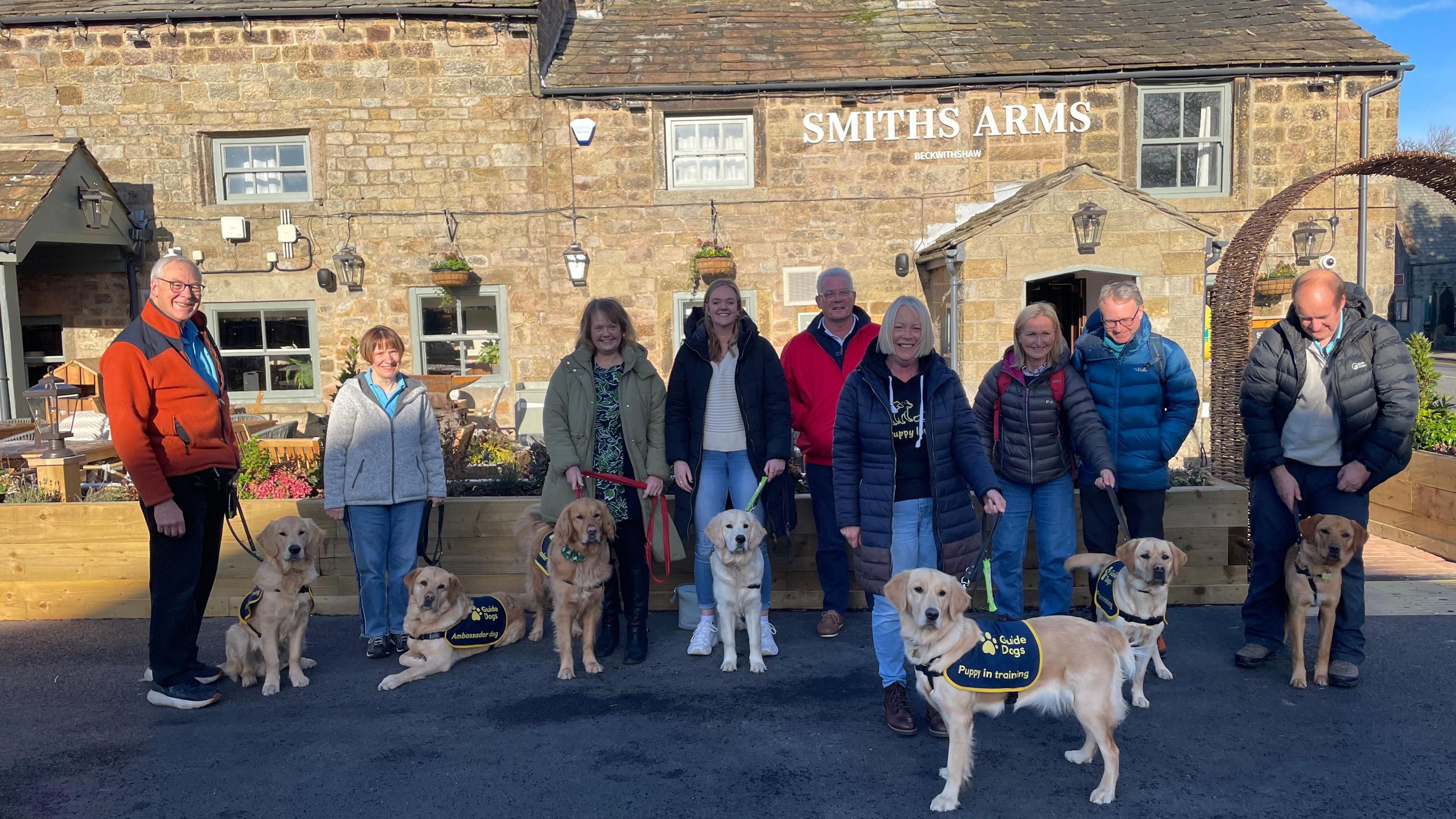 A group of people and golden retrievers outside a pub.