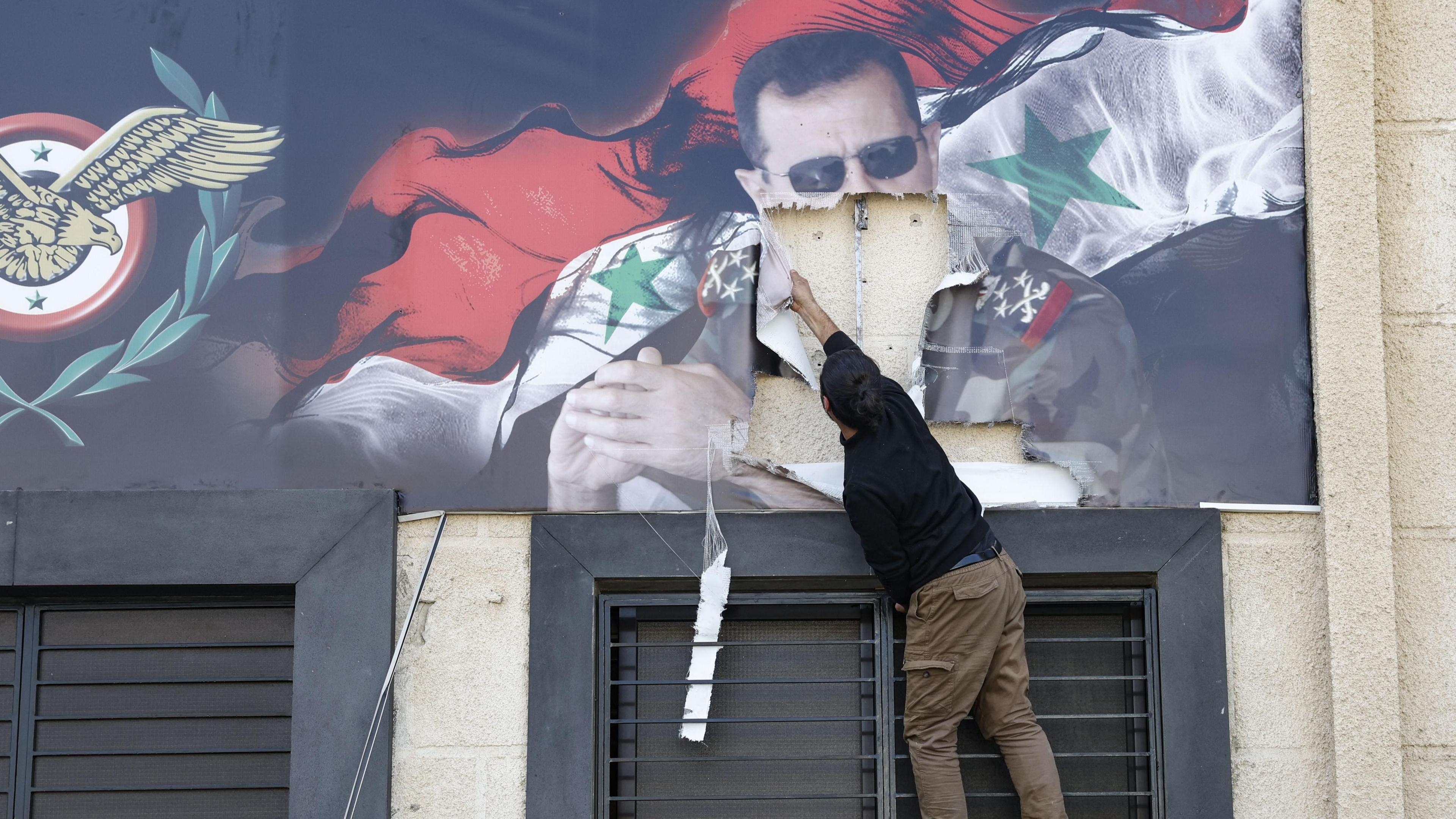 A man tears down a banner showing Bashar al-Assad and the Syrian flag at Mezzeh airbase, on the outskirts of Damascus (16 December 2024)