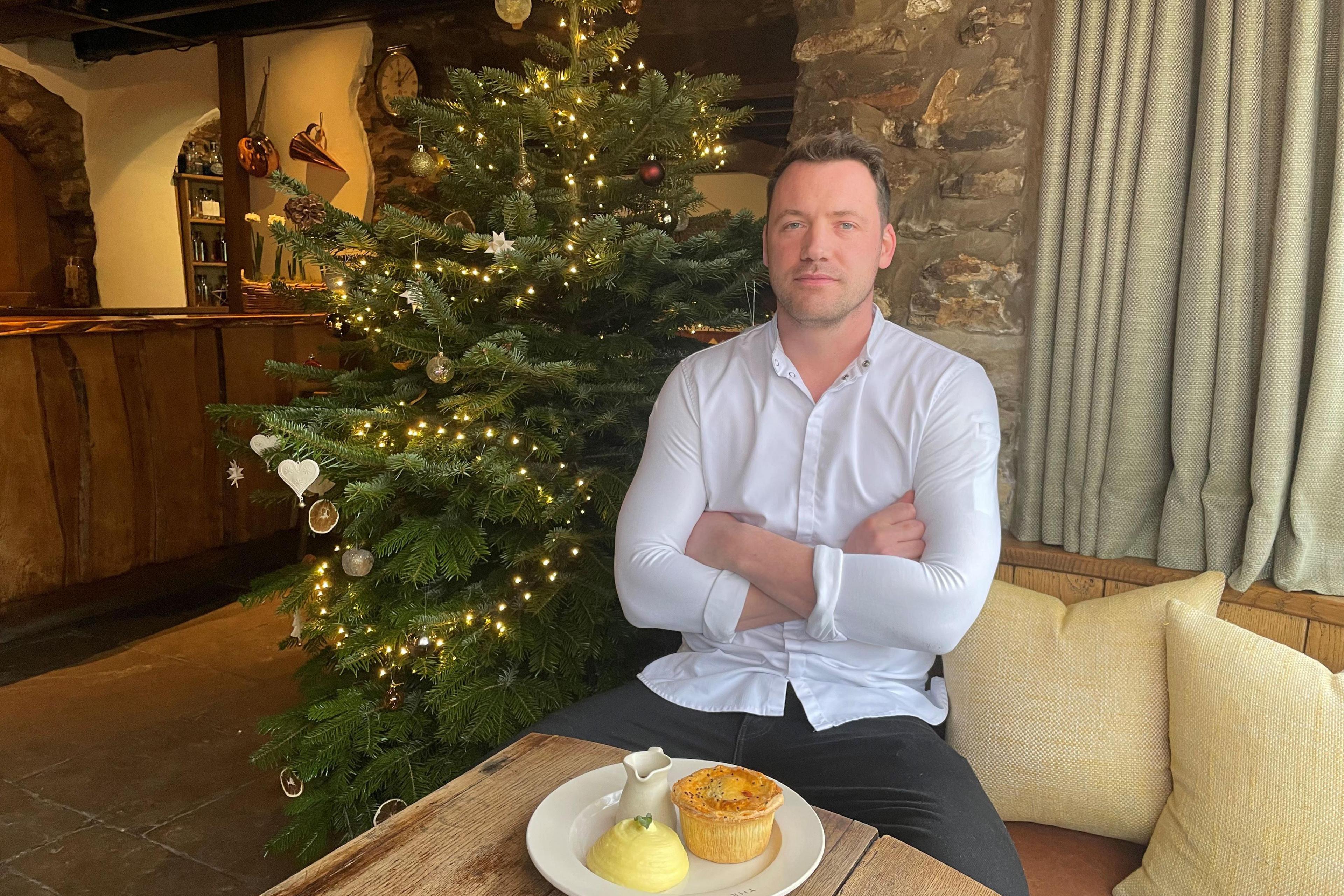 Tommy Banks, pictured in front of a Christmas tree with a plate of pie and mash in front of him. Mr Banks is wearing a white shirt and dark trousers and is sitting with his arms crossed.