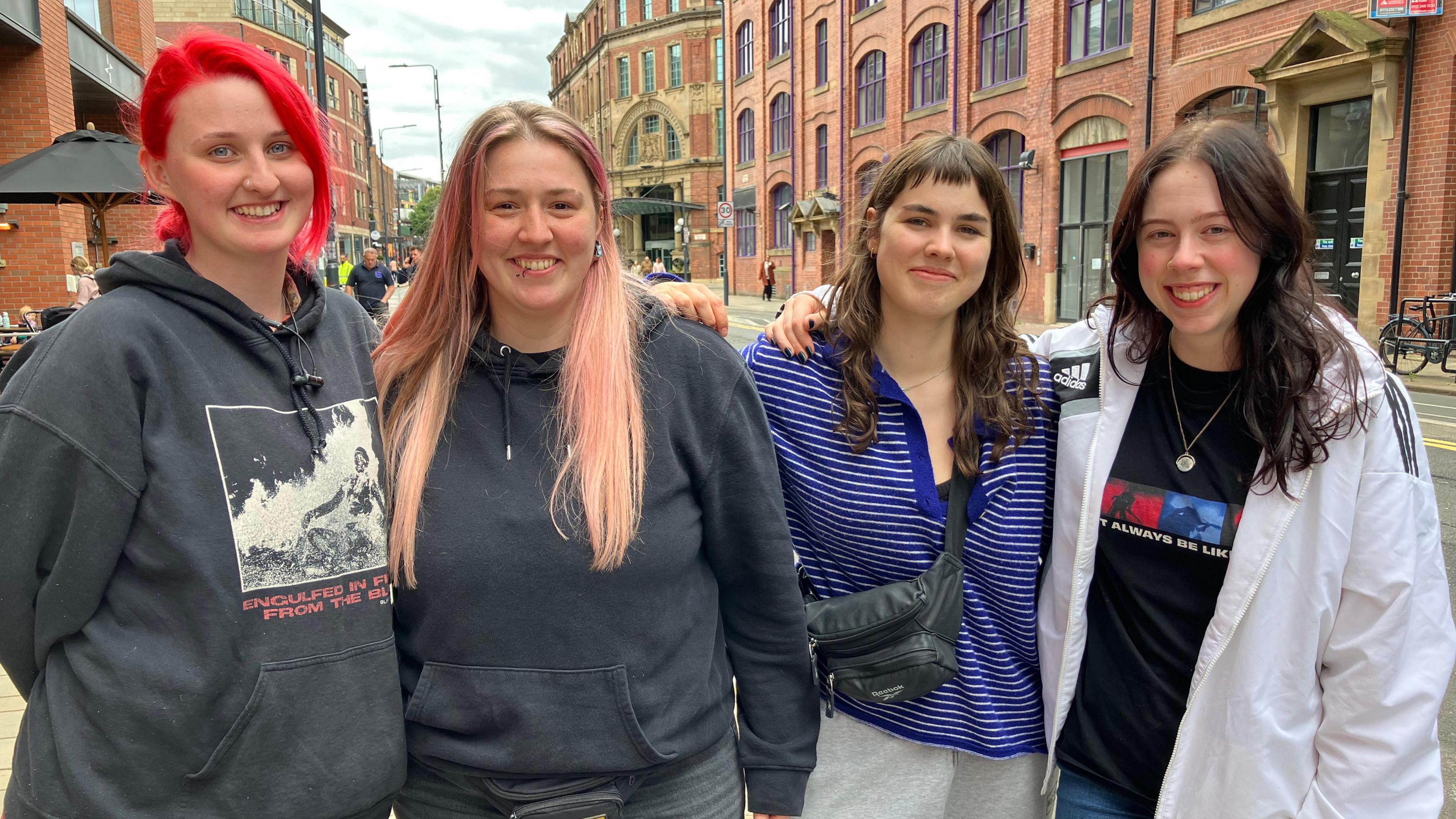 Four women standing together as they head off to Leeds festival, one has red hair and another has pink hair, and two have brown hair.