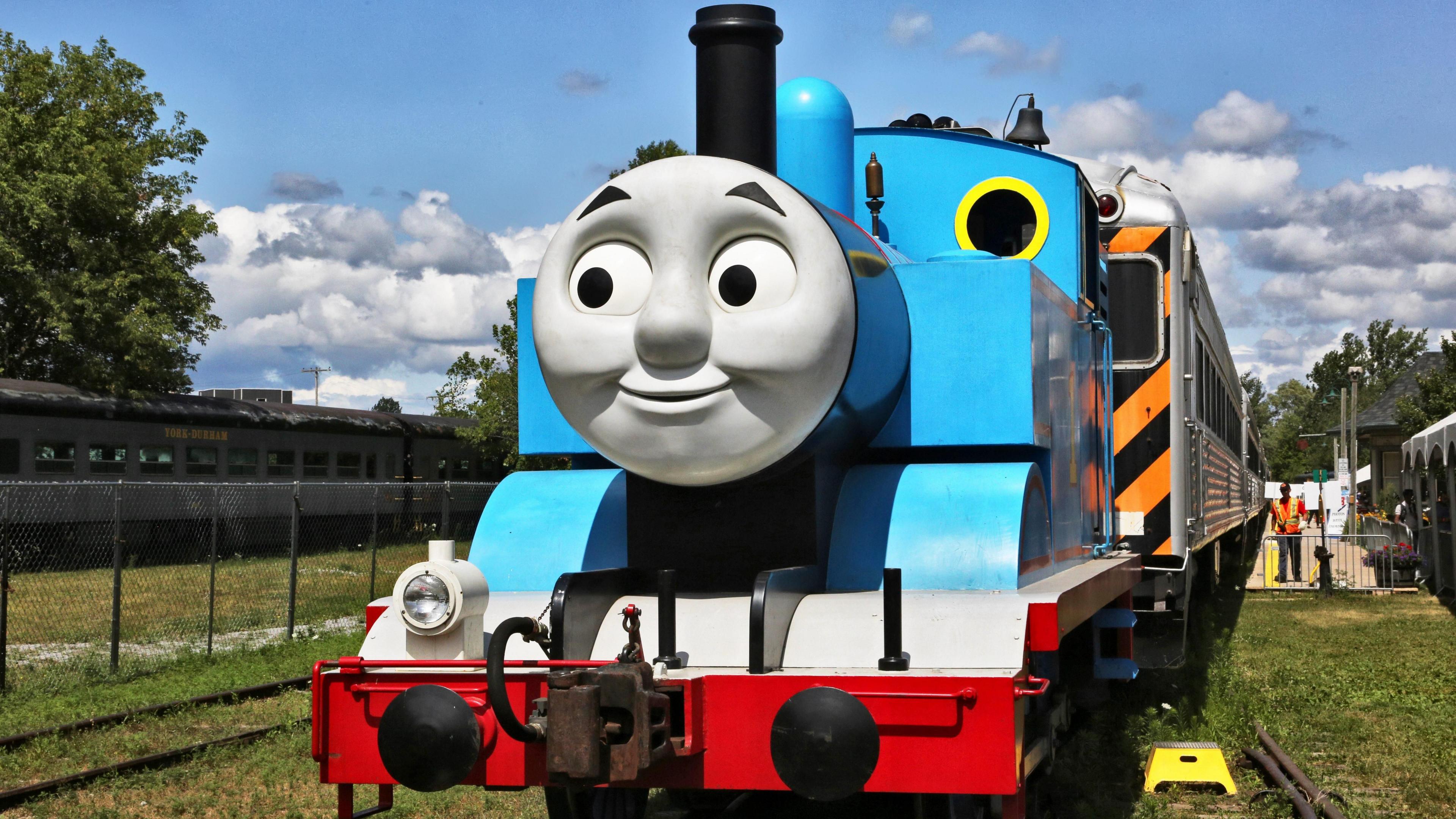 A replica of Thomas the Tank Engine. It is a blue model steam train with a grey smiley face on the front.