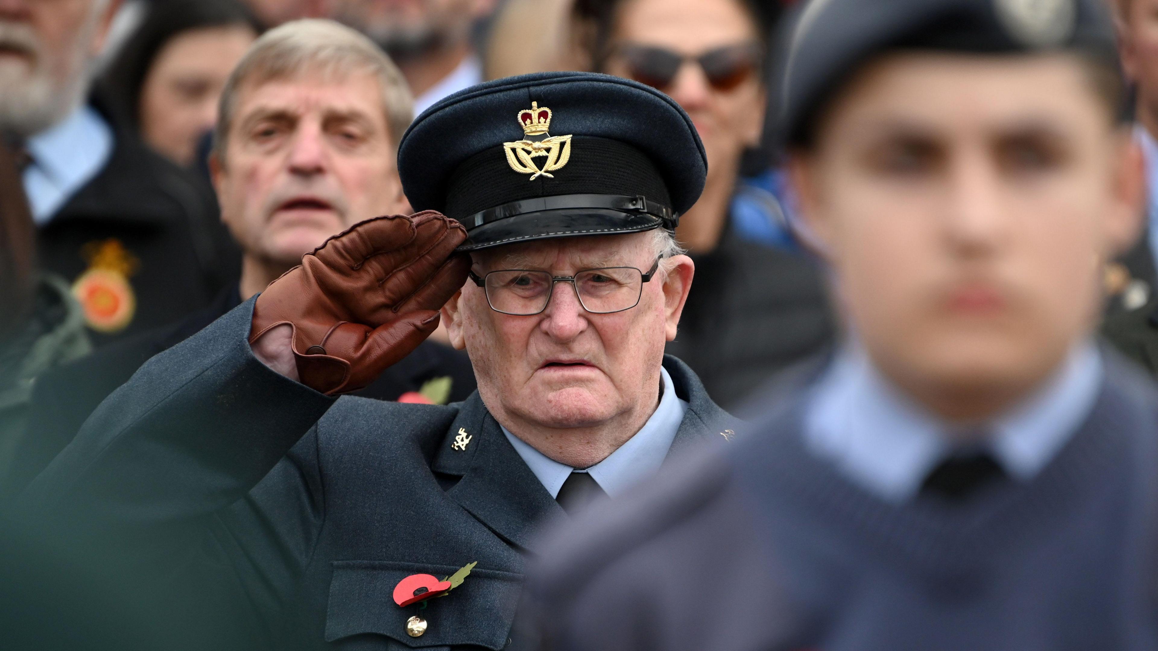 An elderly man wearing a poppy and military cap saluting during the Remembrance Sunday service.