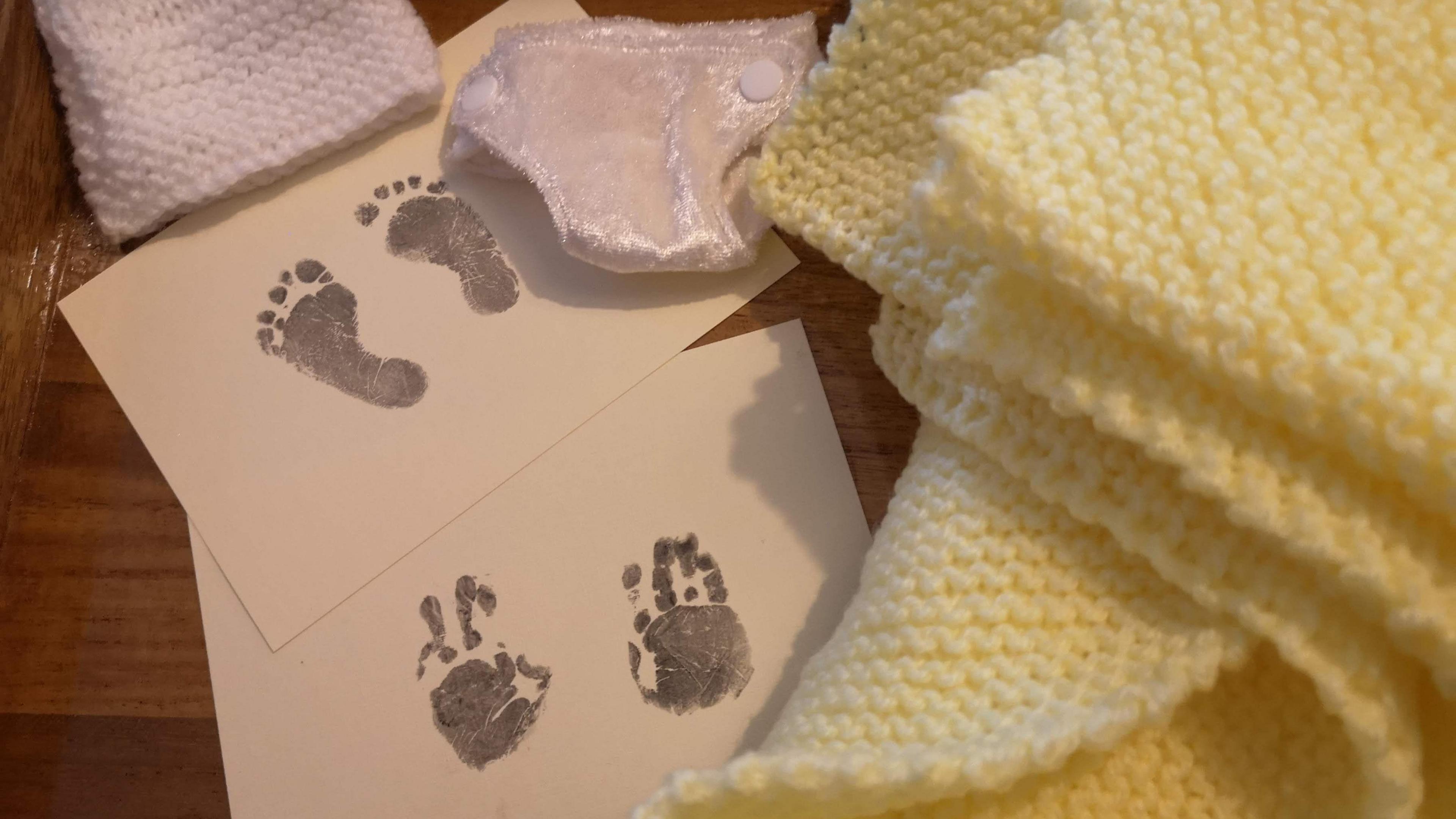 Baby handprints and footprints lies on a table next to a baby blanket