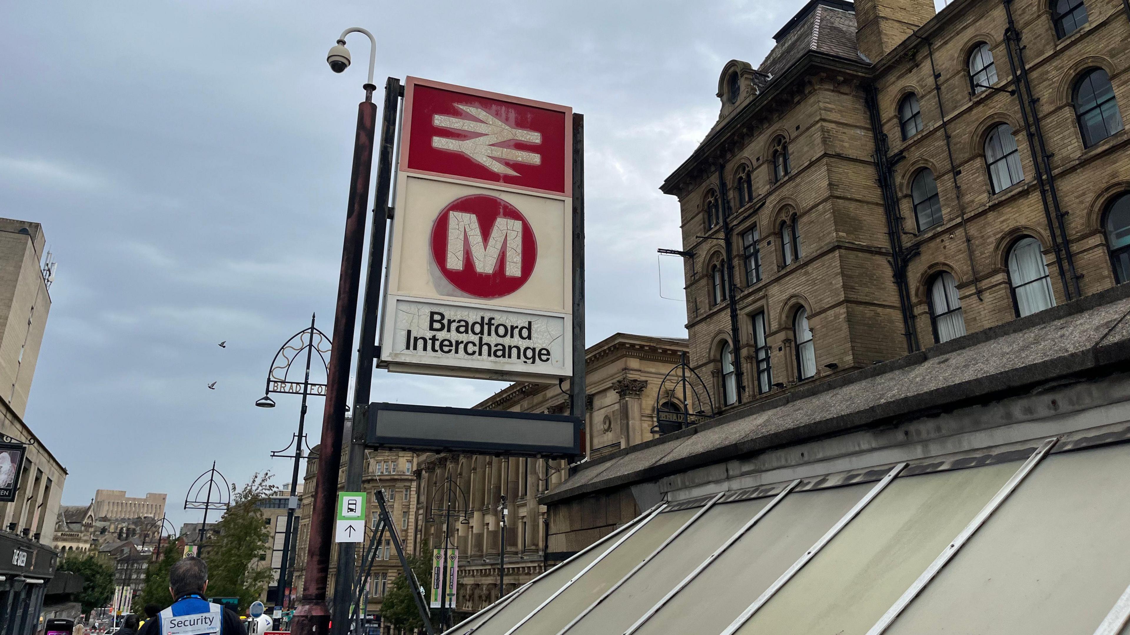 A sign for Bradford Interchange, signposting both rail and bus services. Bradford city centre can be seen in the background, including St George's Hall.