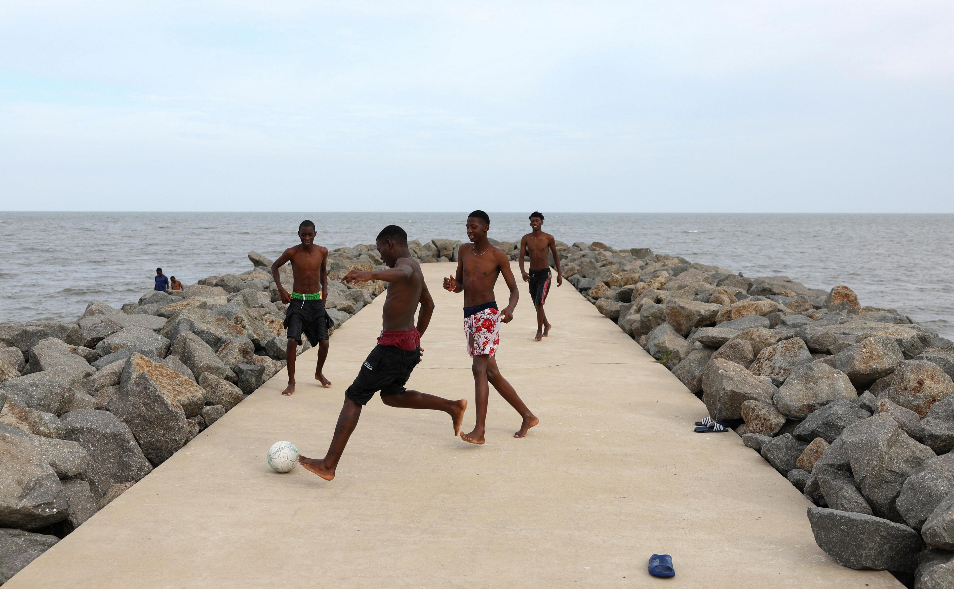 Teenagers play soccer on a concrete beach pathway in Maputo.