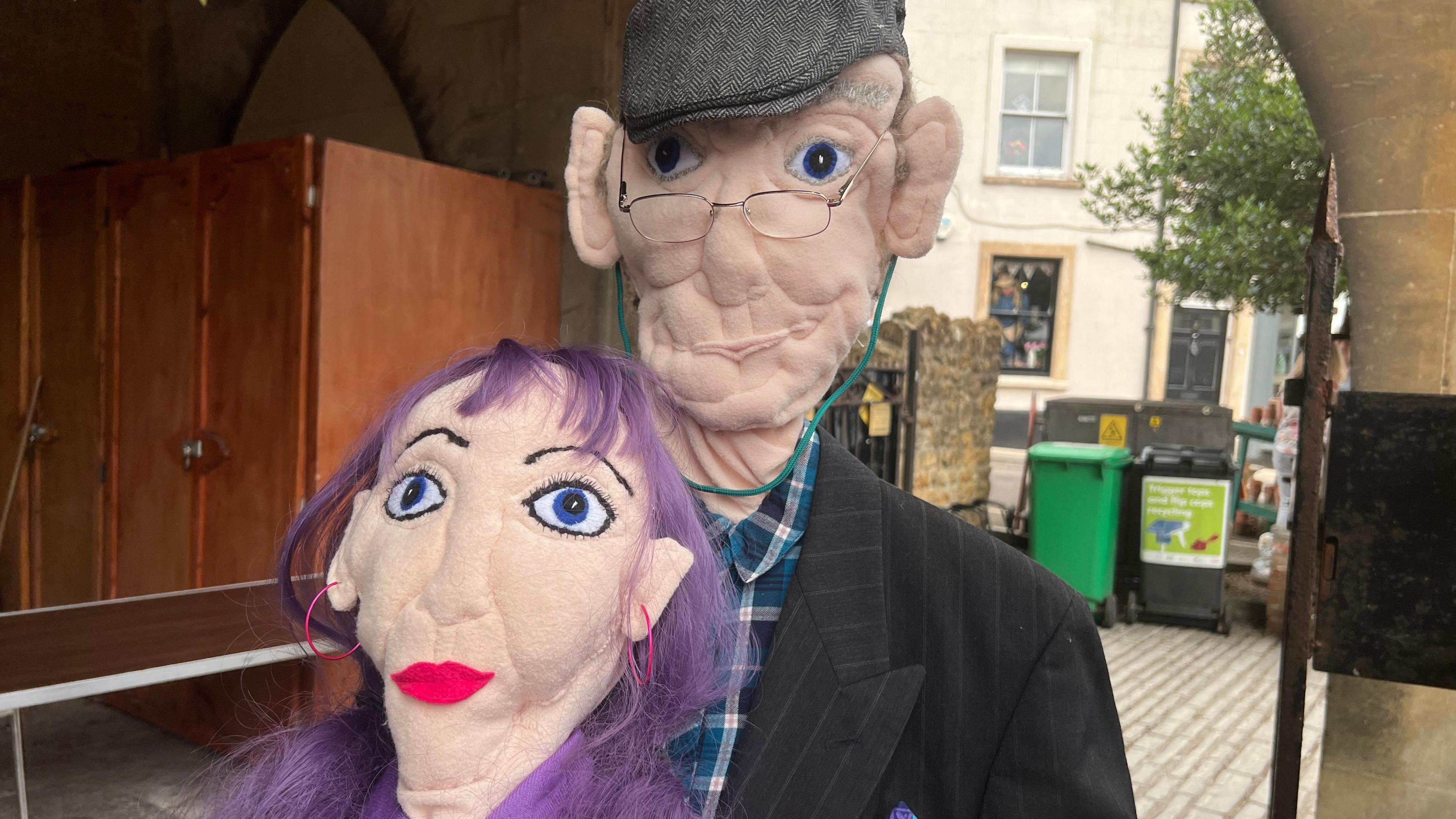 A scarecrow of a woman with purple hair and a scarecrow of an old man