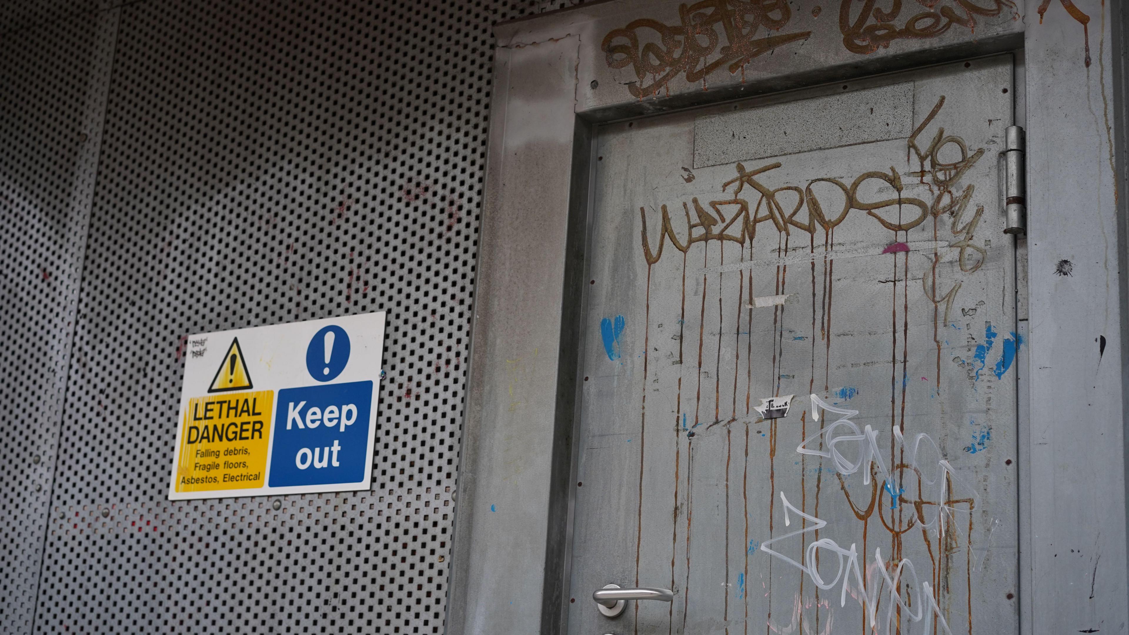 Metal doorway and boarding, the door has graffiti on it and there is a sign saying "LETHAL DANGER KEEP OUT".