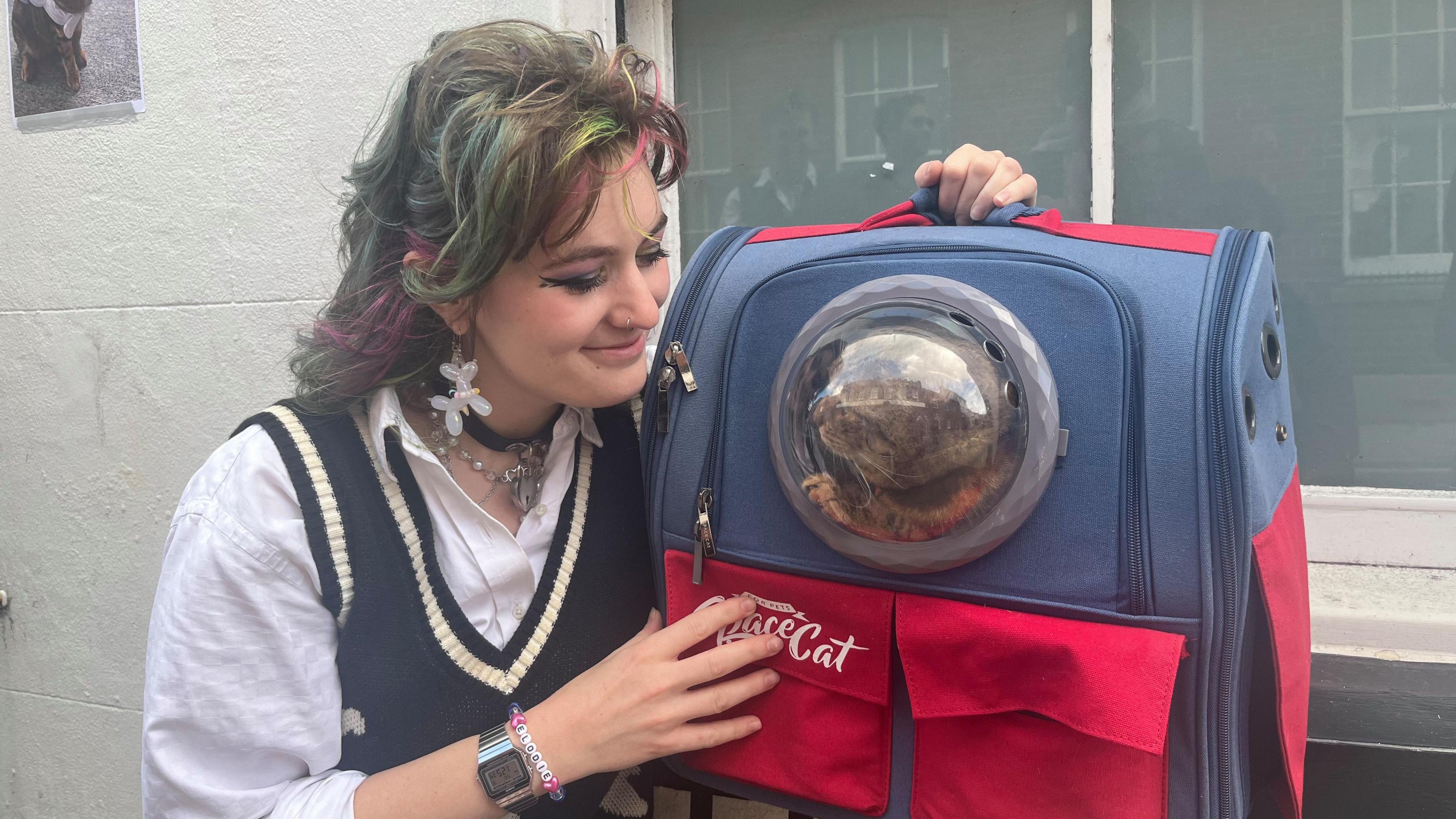 Volunteer Elodie Grenville poses with her cat, Pixie. She looks down at her affectionately. Pixie stares back at her from the window inside its rocket cat carrier.