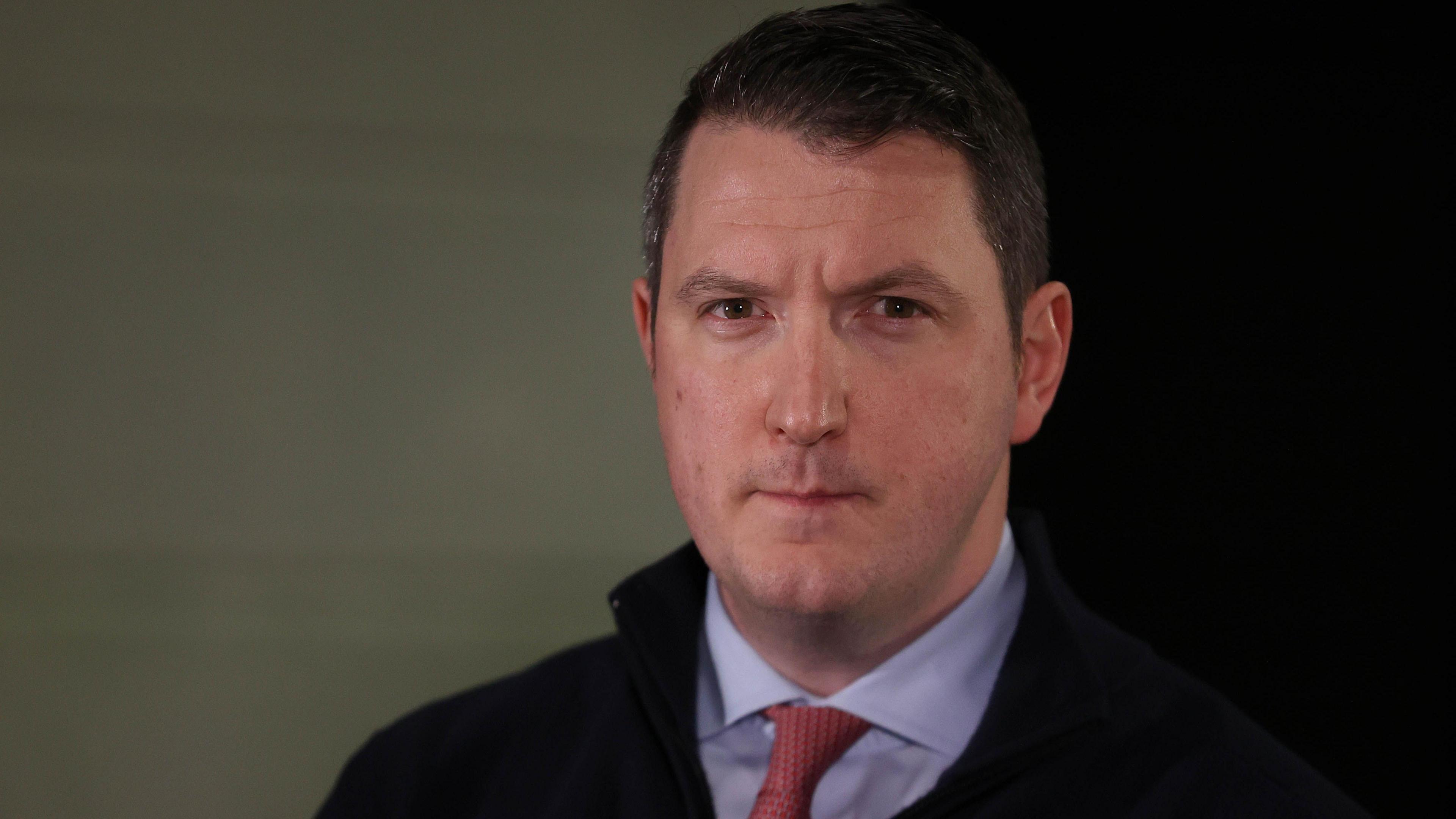 John Finucane is looking into the camera. He's wearing a navy jacket with a blue shirt and a red tie.