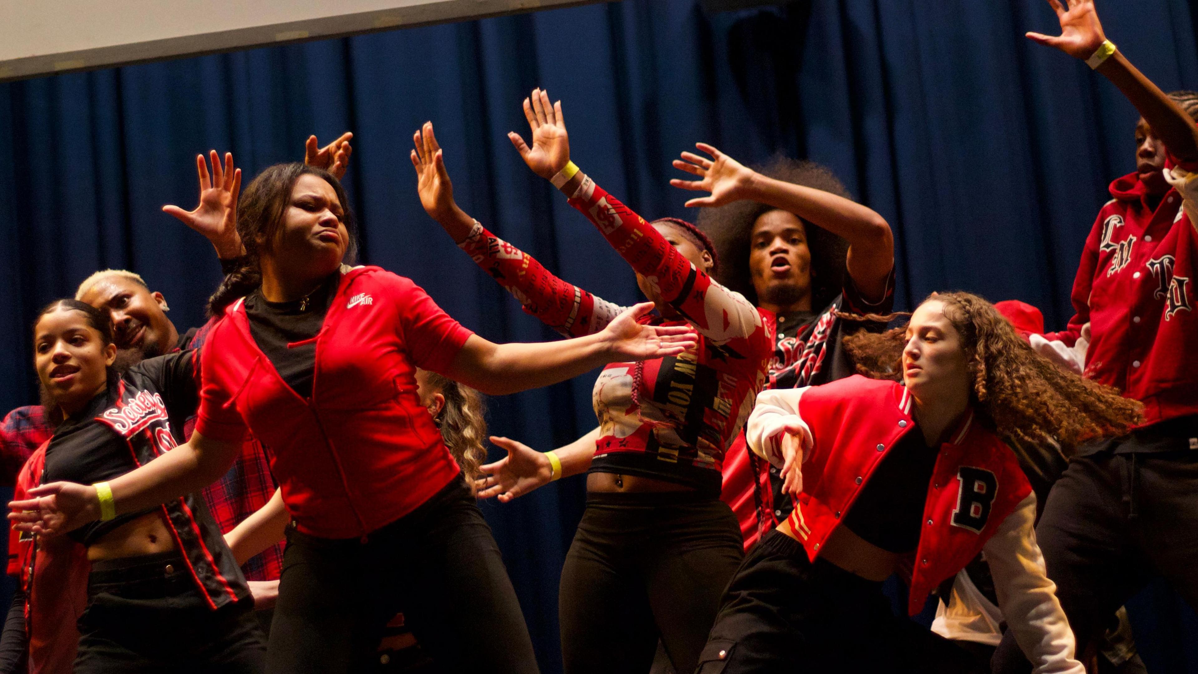 A group of young people, wearing red tops and black trousers, dancing in the talent show Boroughs United