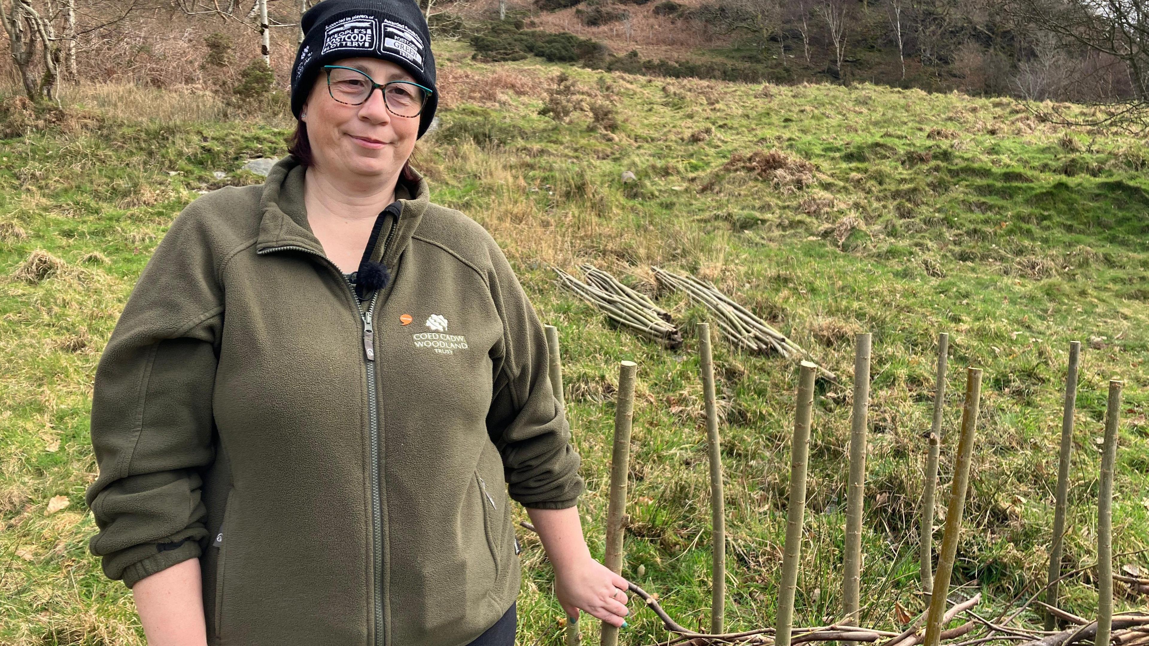 Llun o Llinos Humphreys - llefarydd Coed Cadw - yn sefyll ar ochr bryn ger Tal-y-bont yng Ngheredigion. 