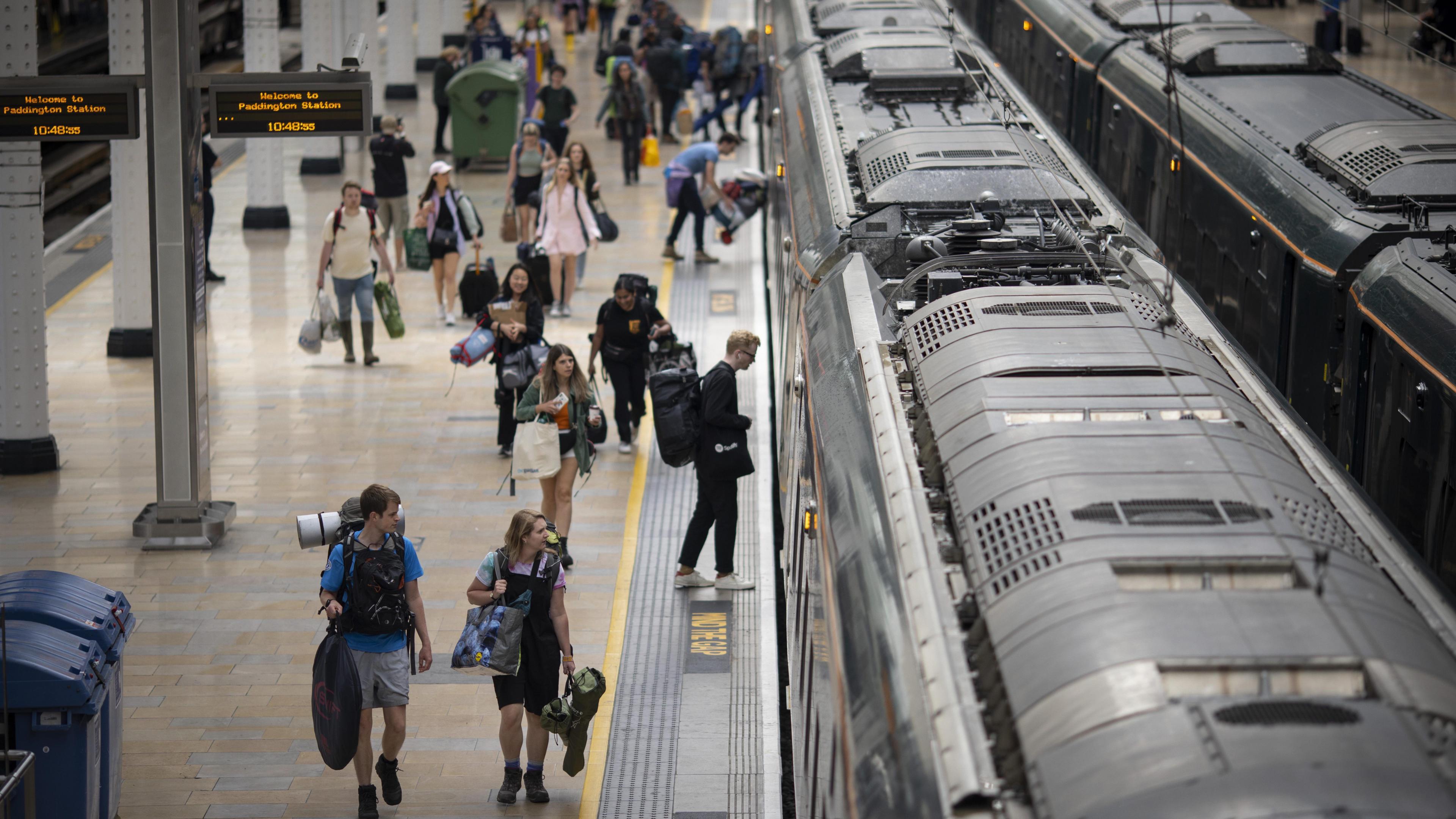 Image of Glastonbury attendees boarding a train at London Paddington. Many people are carrying large bags and camping equipment