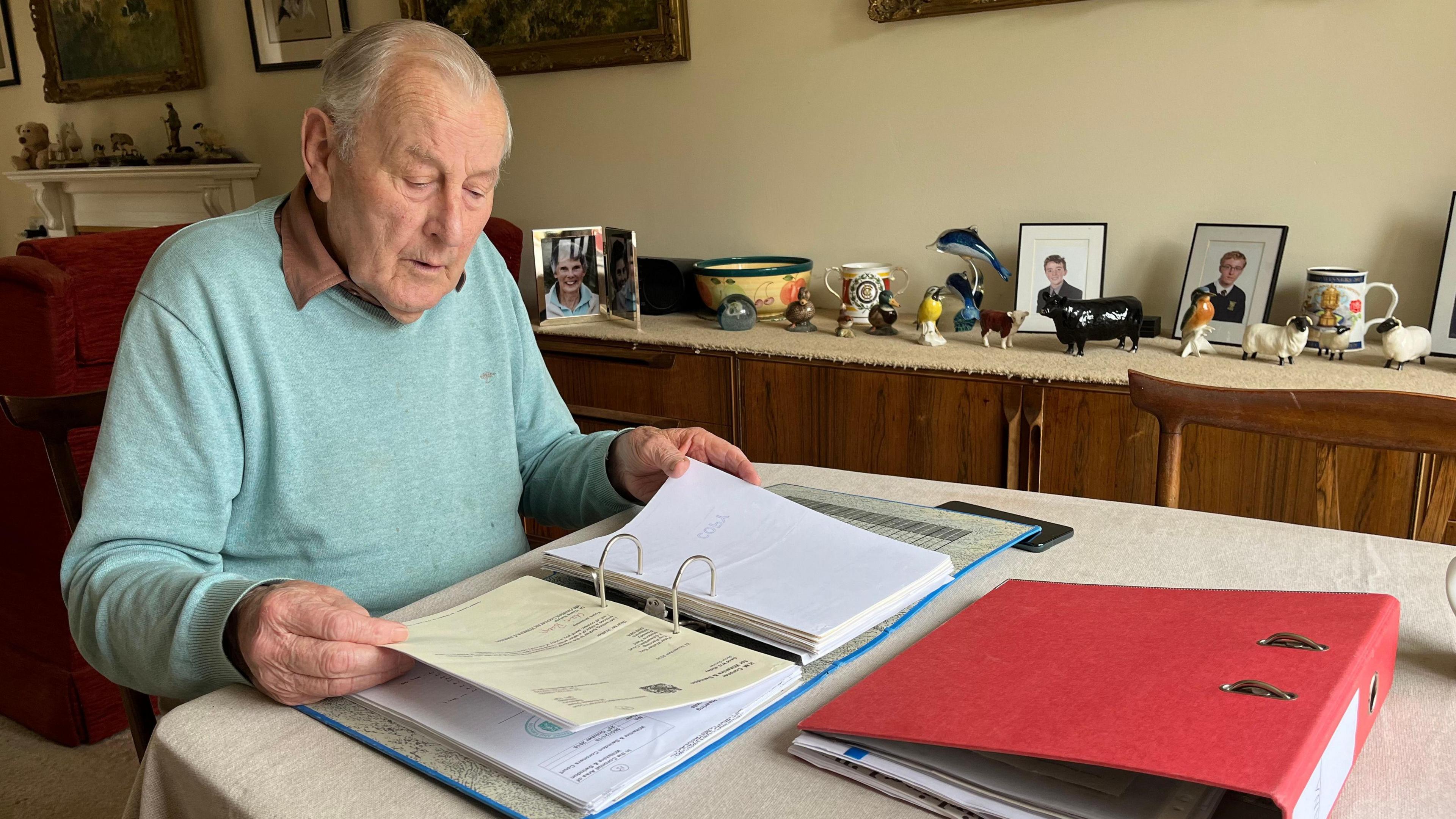 Peter Walker is sititng at his dining table and looking through a folder