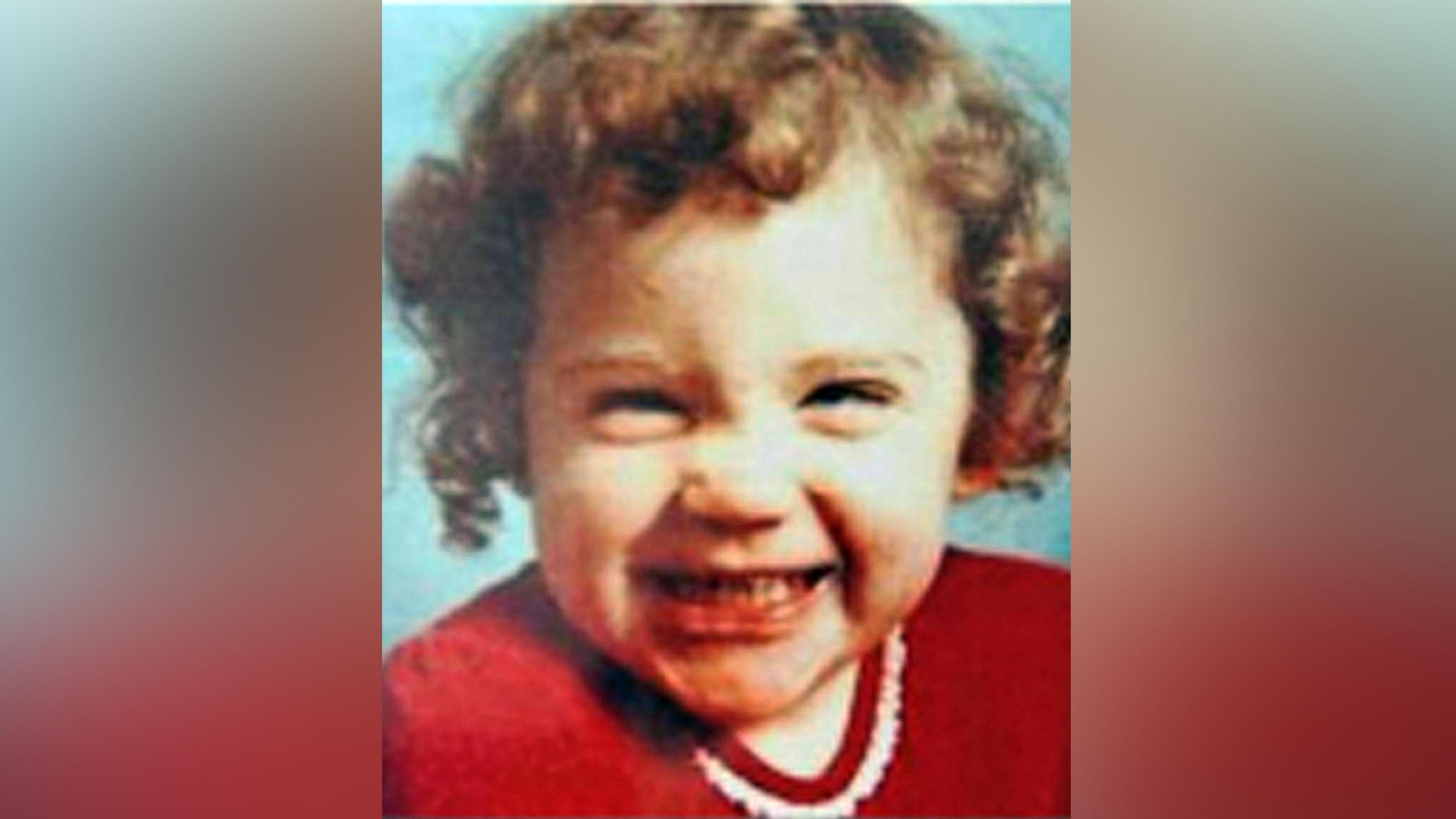 Katrice Lee gives a big smile to the camera. She has dark curly hair and is wearing a red top.