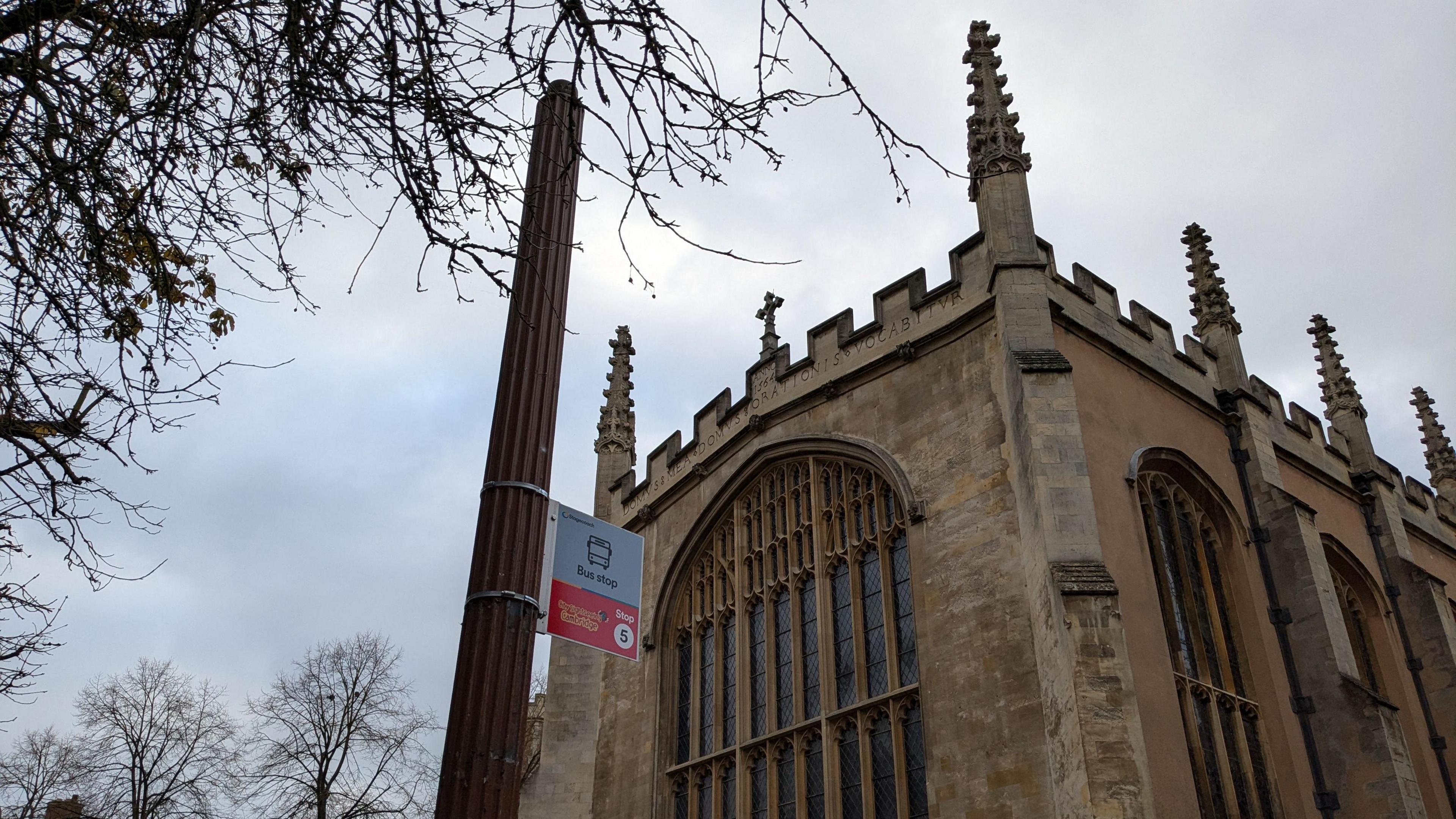 View of St John's Street in Cambridge showing a street light without a lantern at the top. There is a bus stop sign attached to the post and an ornate church in the background