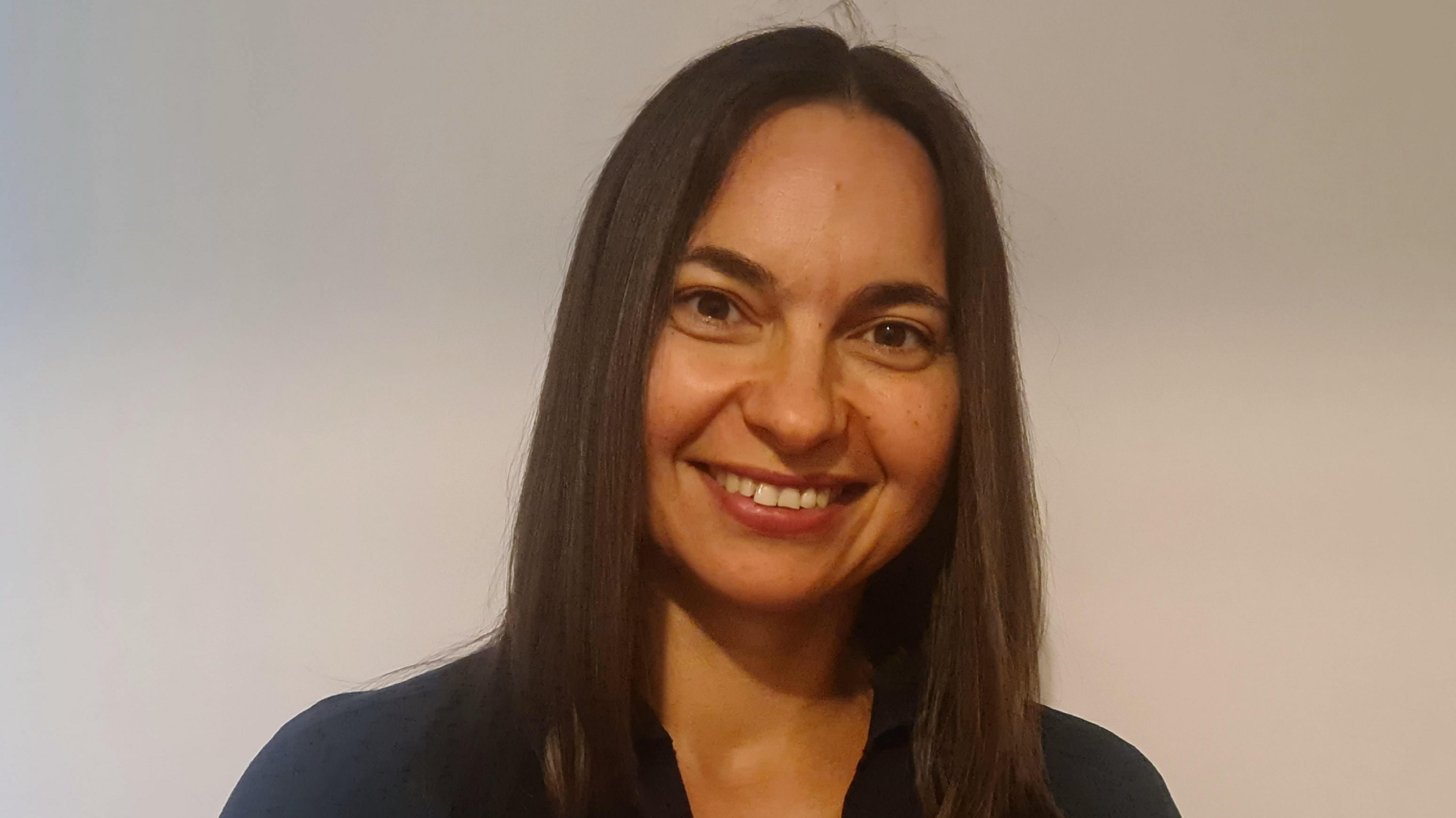 Oksana Koryak, looking straight at the camera and smiling. She has long dark hair and a dark top. 