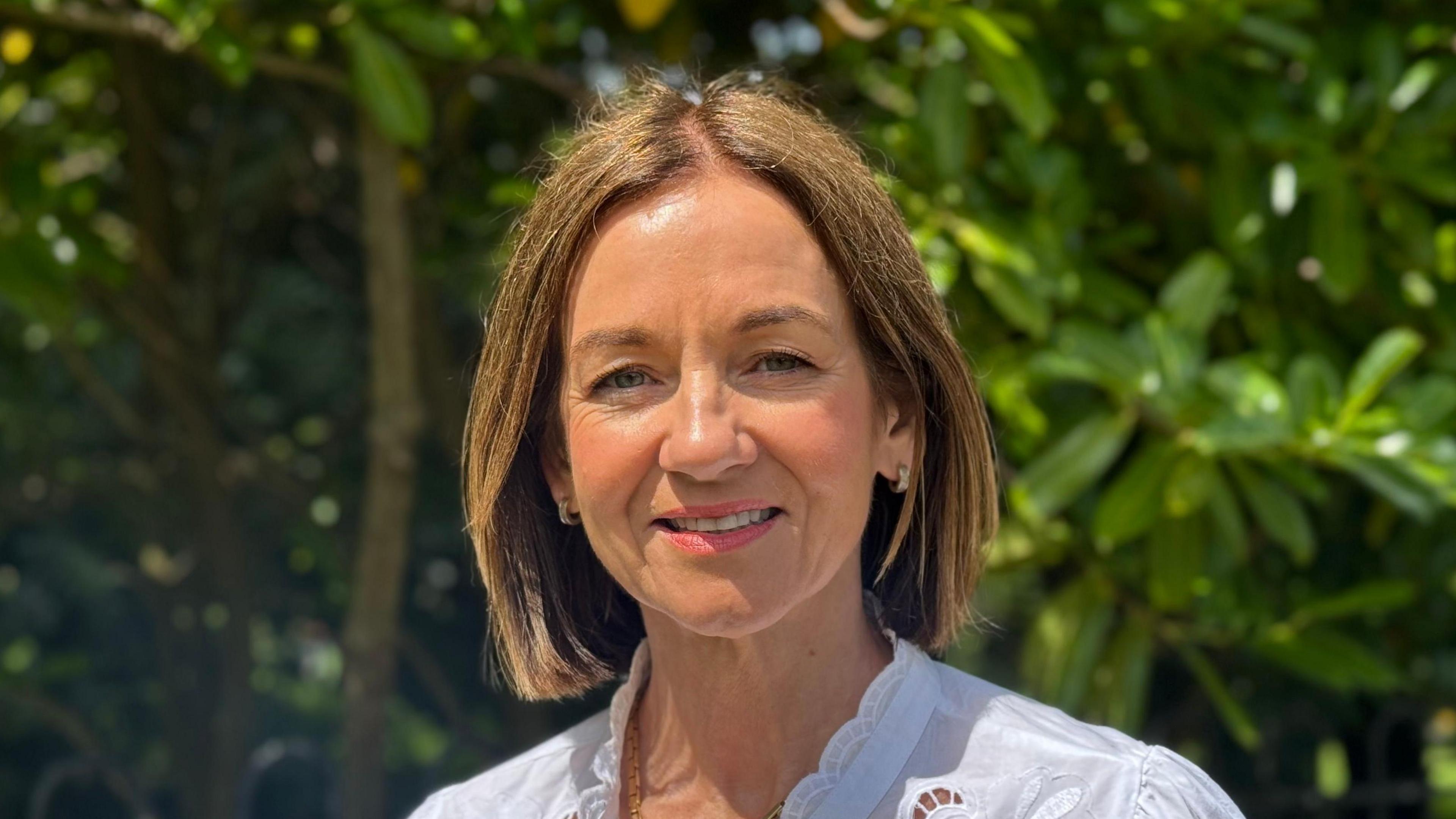 Councillor Gillian McCollum has short brown hair and is smiling at camera. Greenery in background.