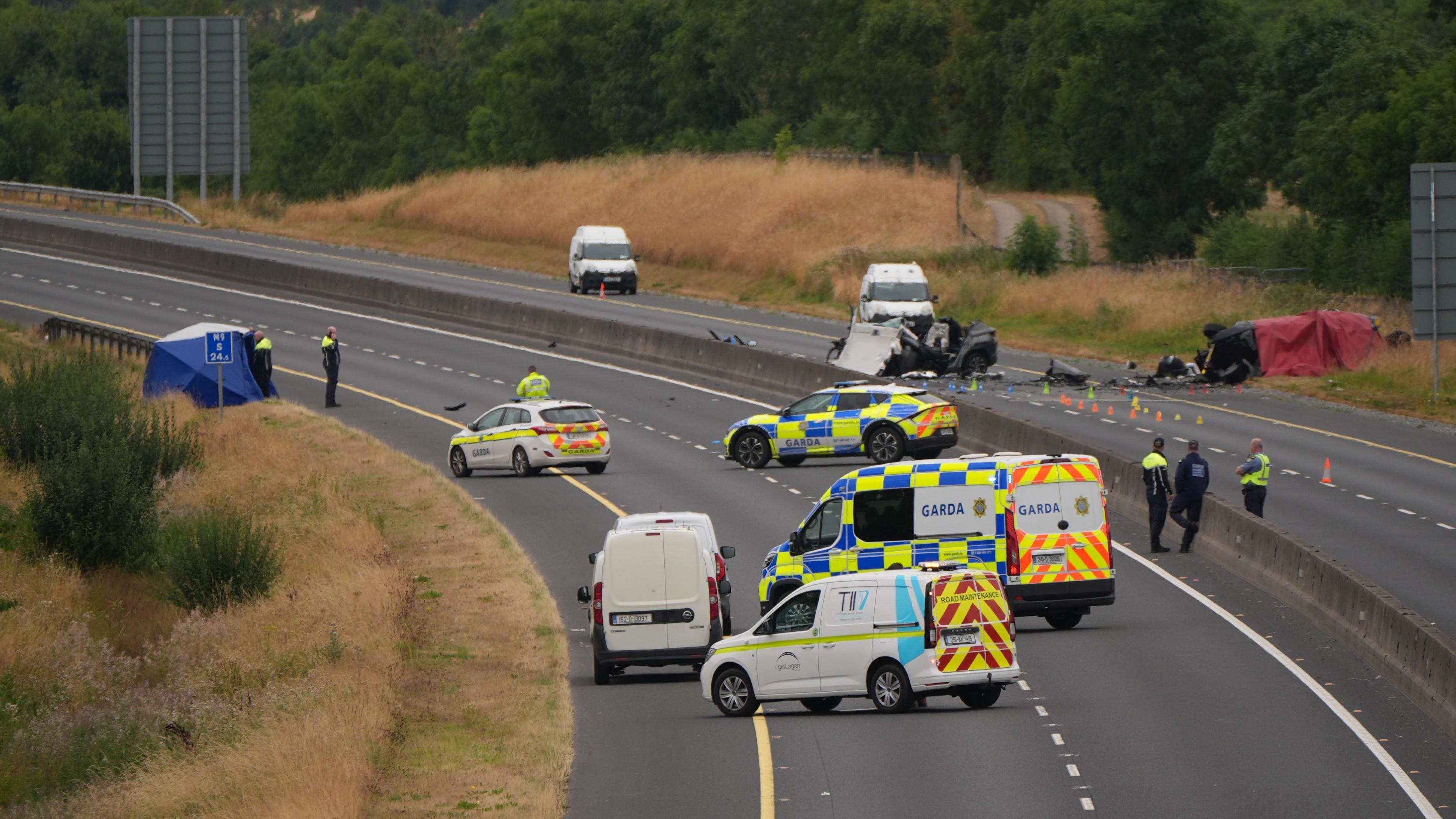 A shot of a car crash site showing a section of closed motorway with many emergency service vehicles on the road and debris from the crash.