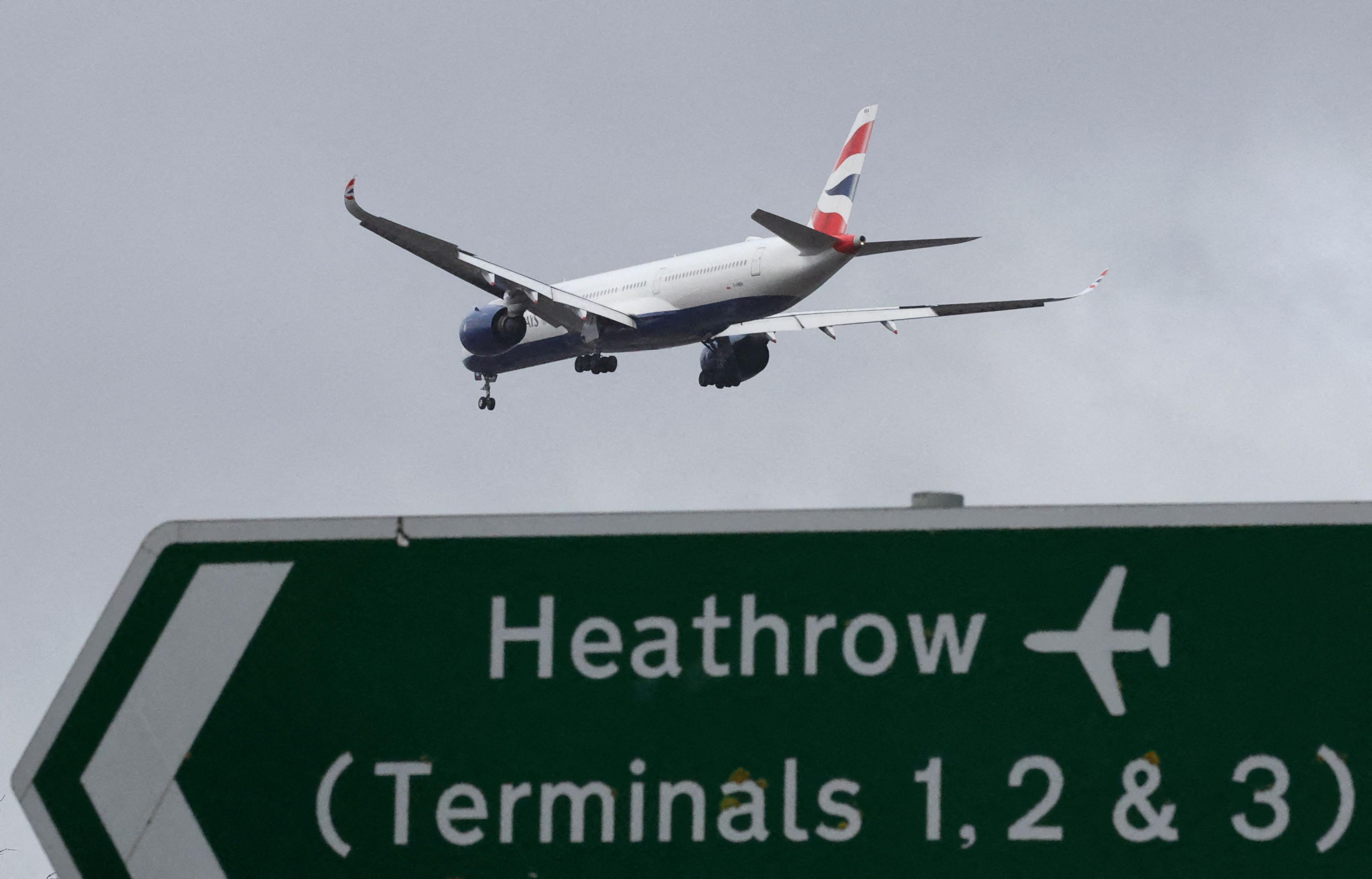 British Airways plane flying in the sky with a green and white sign pointing towards 'Heathrow terminals 1,2 & 3'