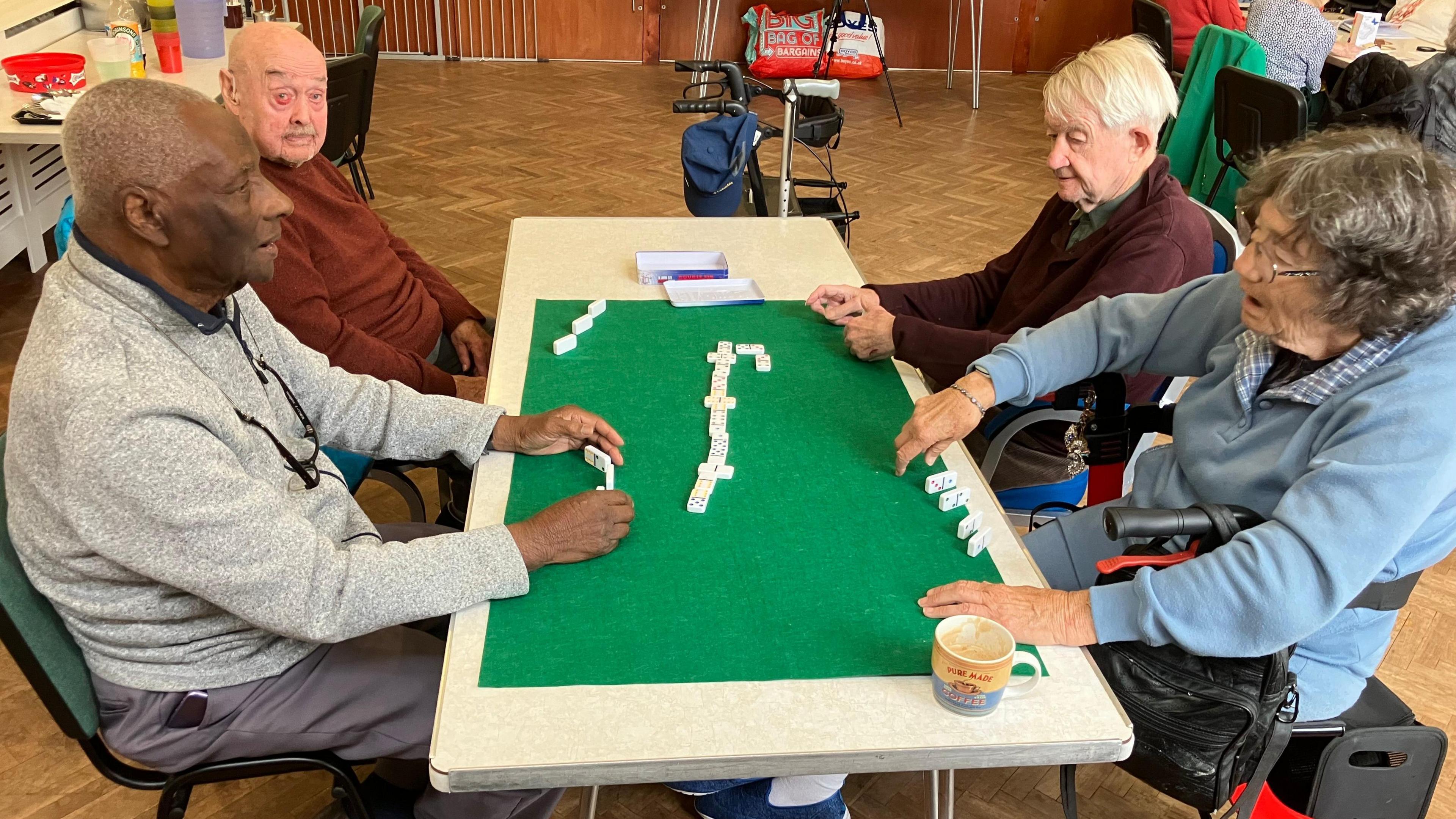 Four older people sit around a table playing dominoes