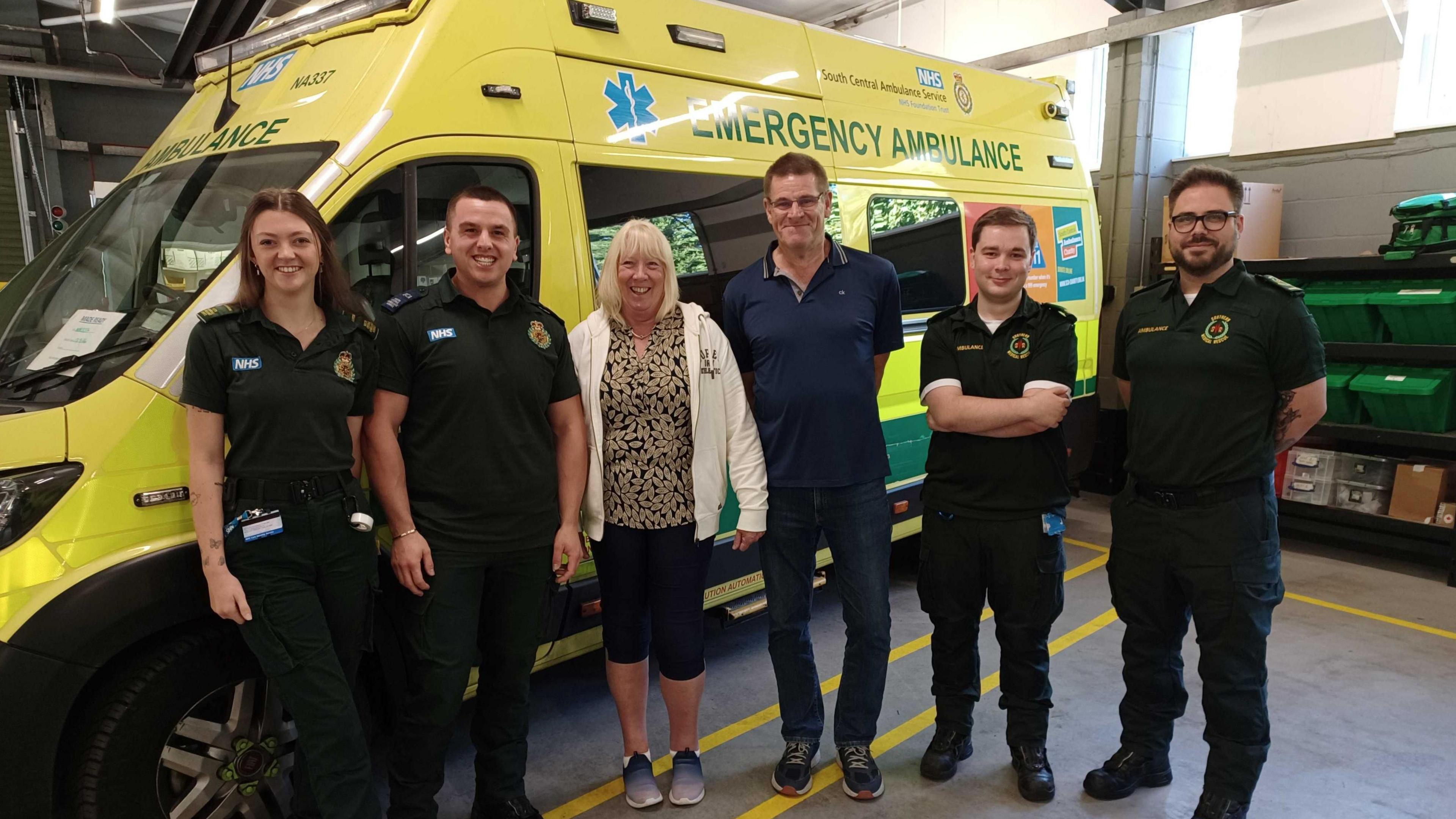 (L-R), Caitlyn, Sam, Wendy, Dave, Kieran and Craig. Caitlyn, Sam, Kieran and Craig wearing paramedic uniform whilst Wendy is wearing black cropped trousers, a leopard print top and white zip jacket and her husband Dave standing to her right is wearing blue jeans and a blue polo shirt.