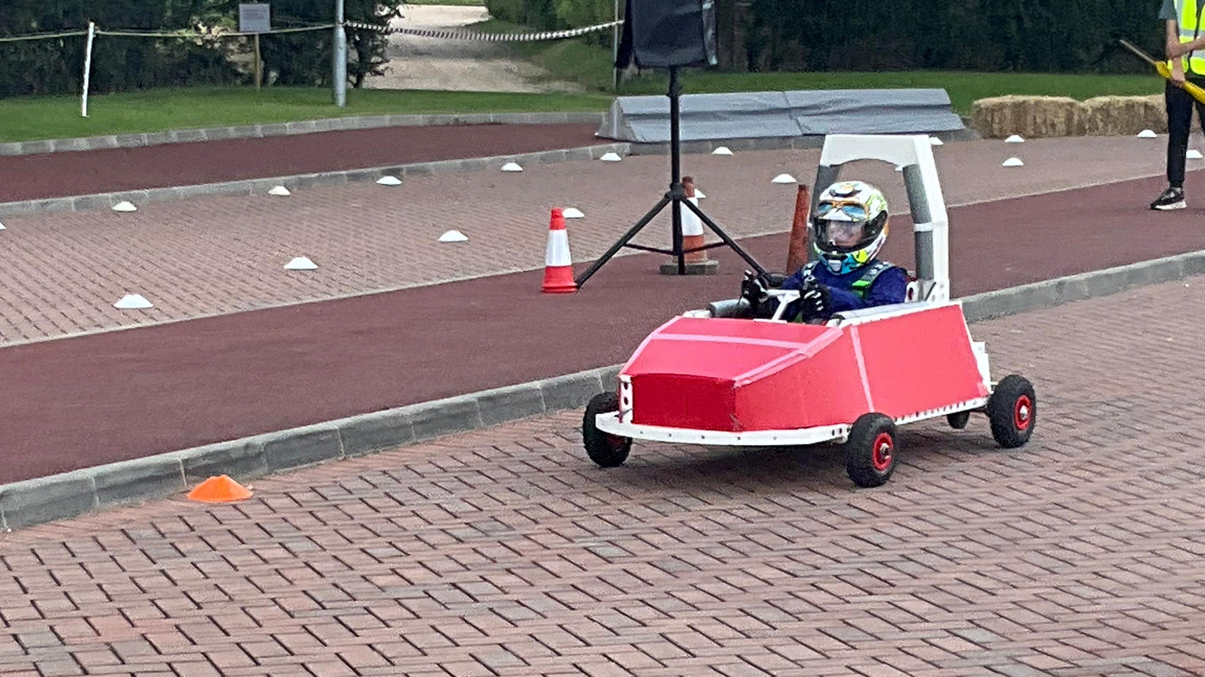 A pupil drives one of the electric go-karts, while wearing a helmet and protective clothing.