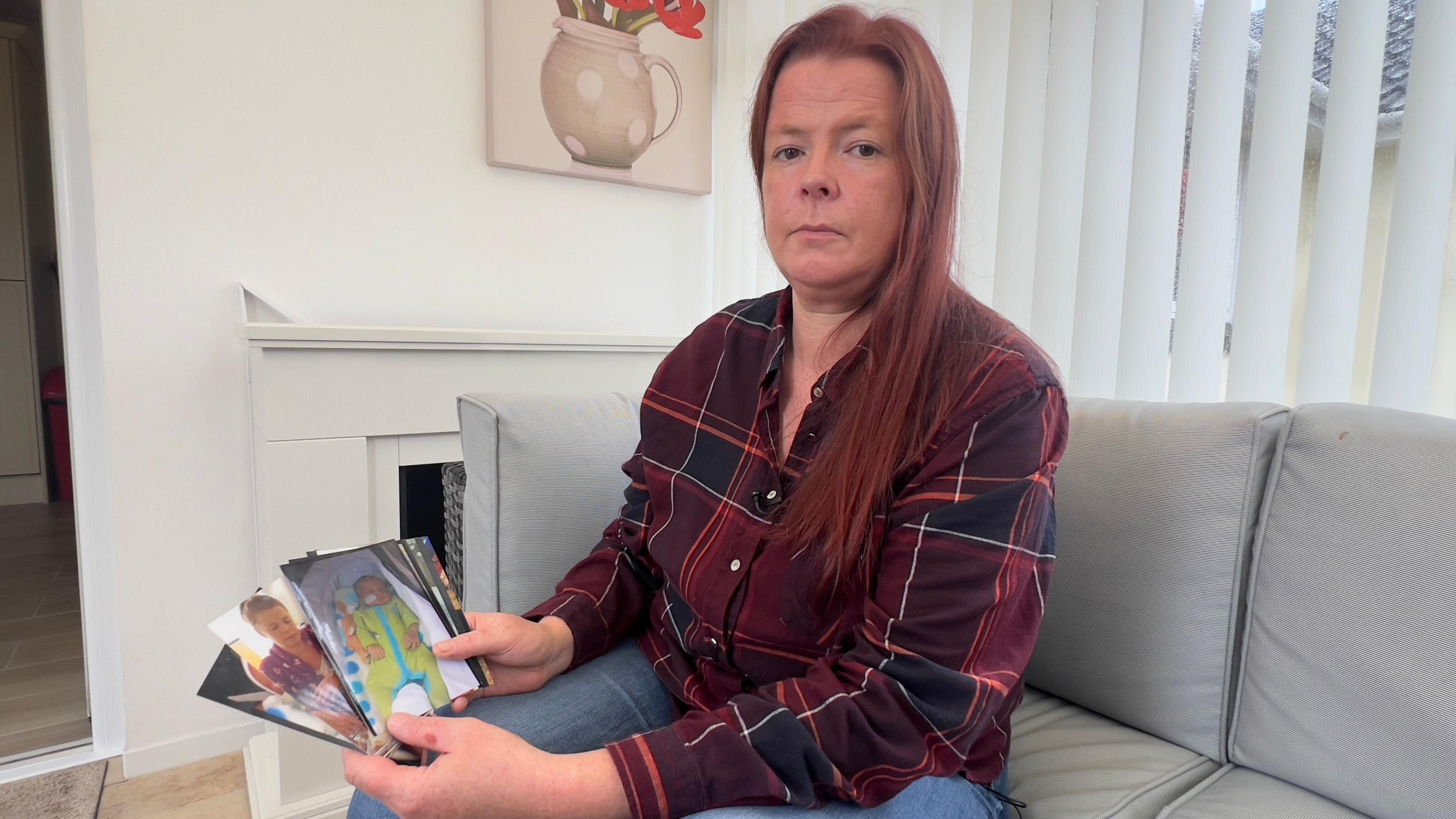 Rachel Kemble, who has long red hair and is wearing a red checked shirt and blue jeans, sat on a cream corner sofa and holding fanned-out pictures of her baby boy