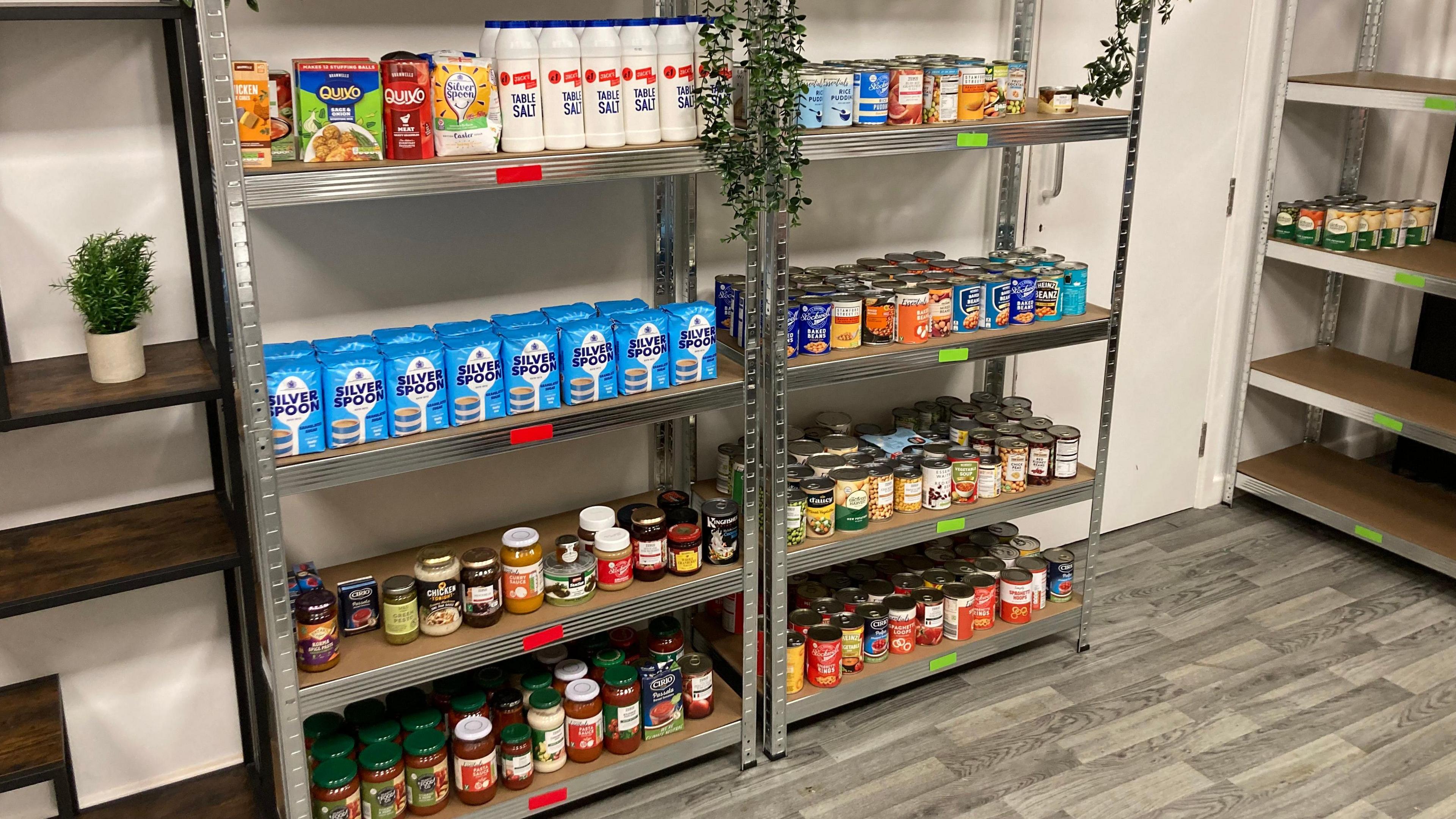 Two shelving units with food on them - including tinned goods and sauces in jars