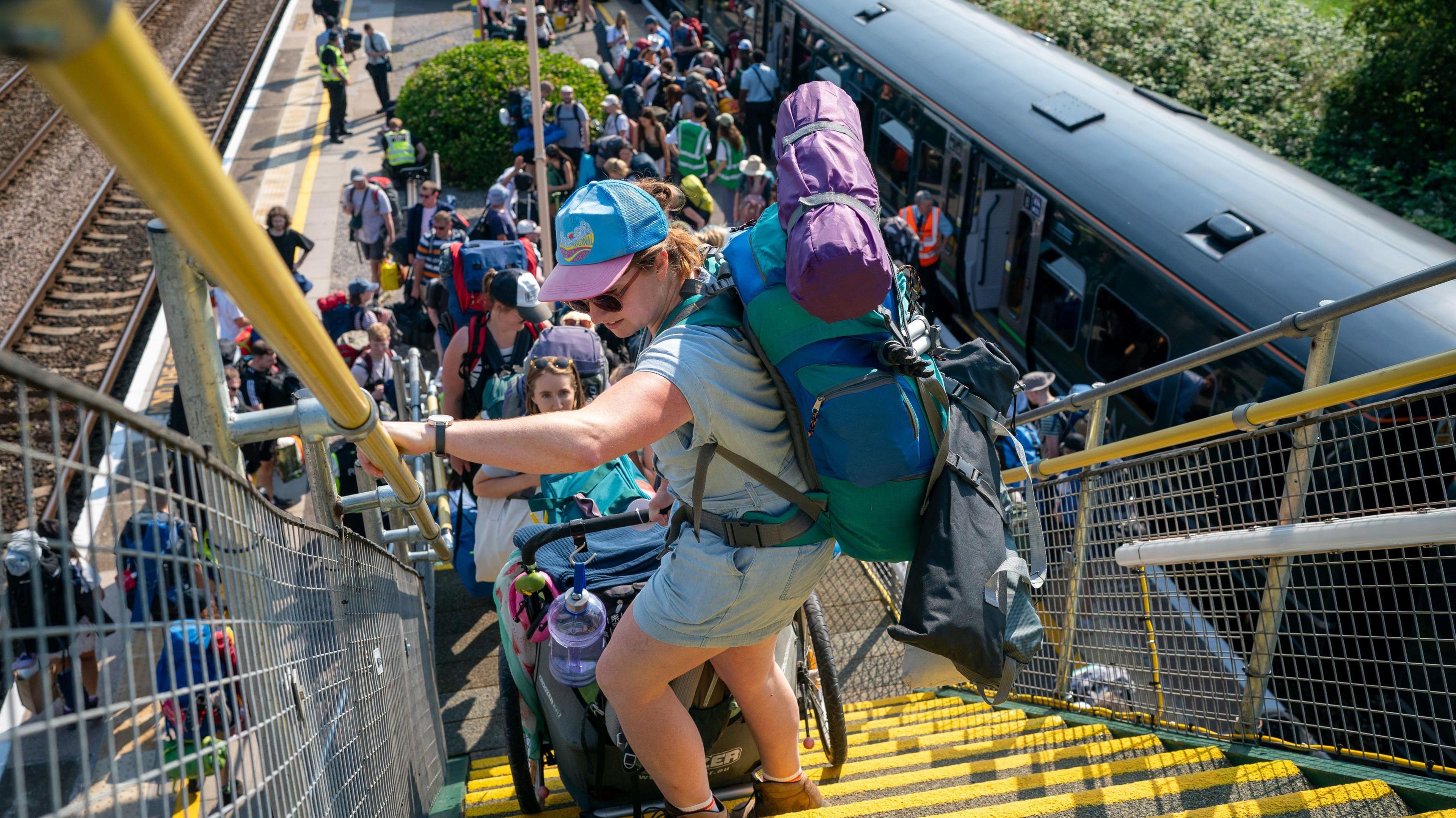 Crowds of people carry heavy bags and trolleys up a railway bridge at Castle Cary. 