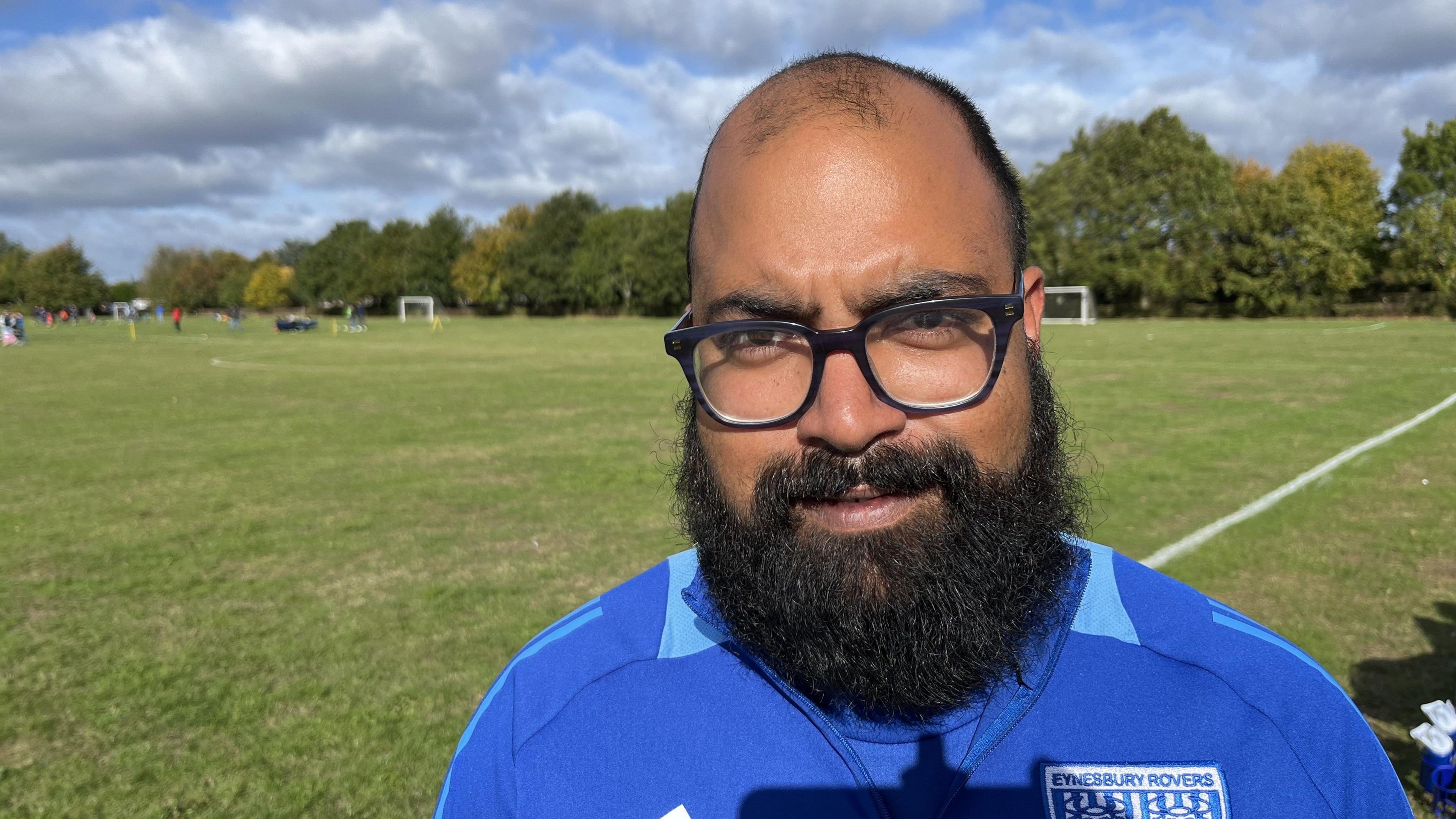 Haani Rasool looks intio the sun - he is wearing a bright blue sport jacket. He has a black beard and is wearing glasses