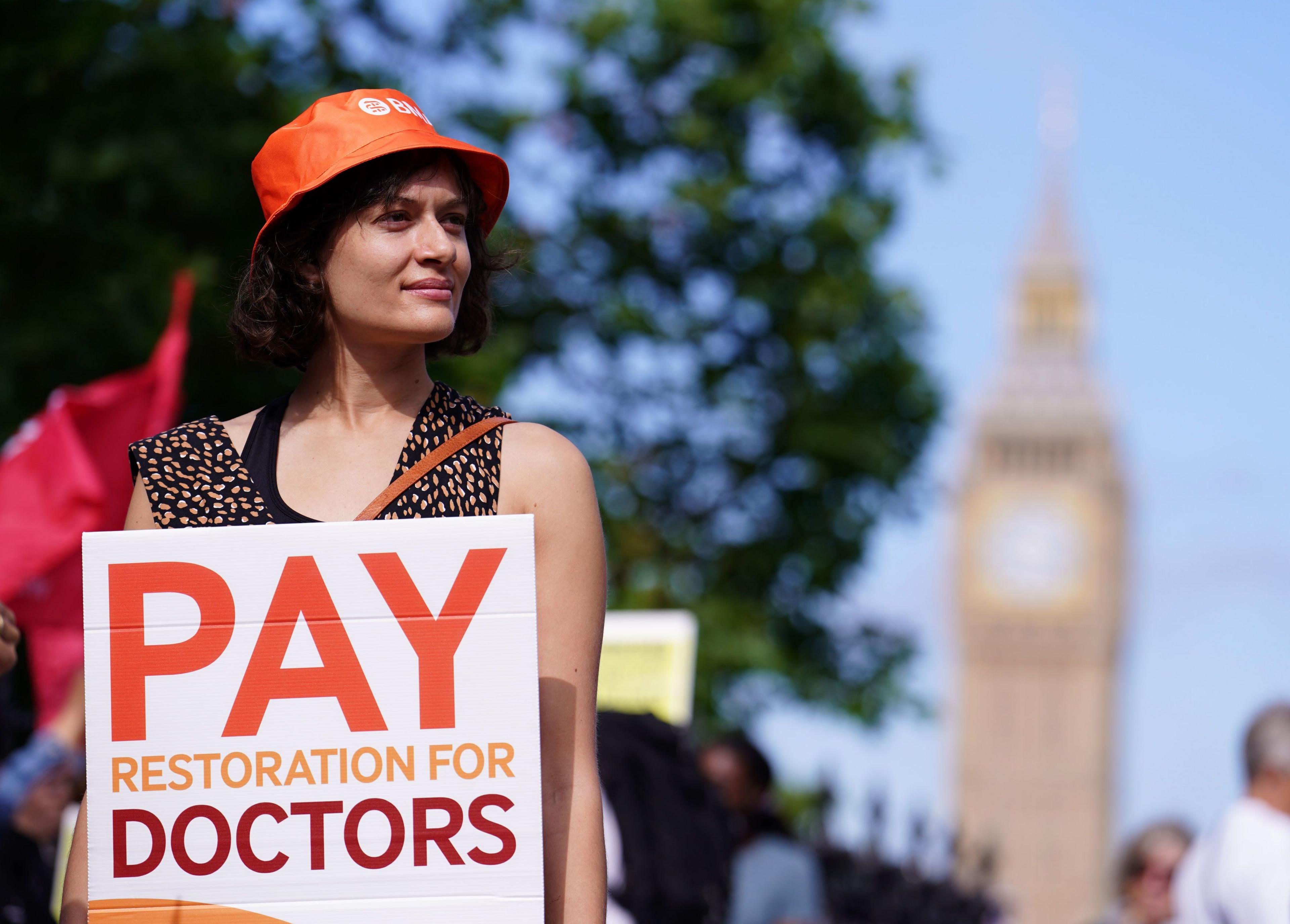 Junior doctor in front of Big Ben holding a sign saying pay restoration for doctors