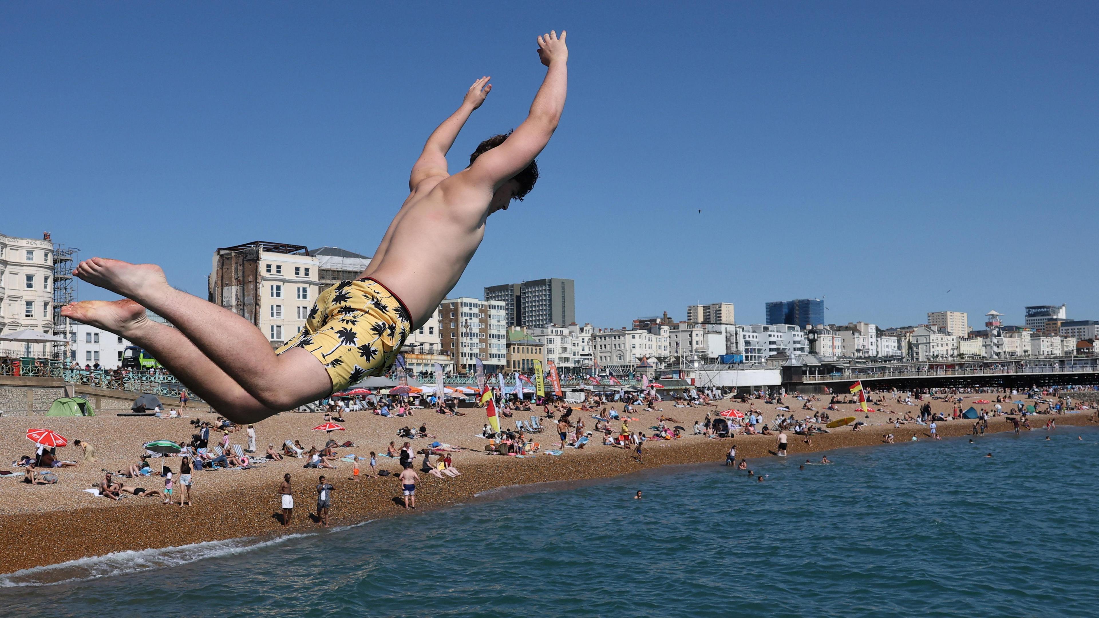 A young man jumps off a seawall into the sea at Brighton seafront on Monday
