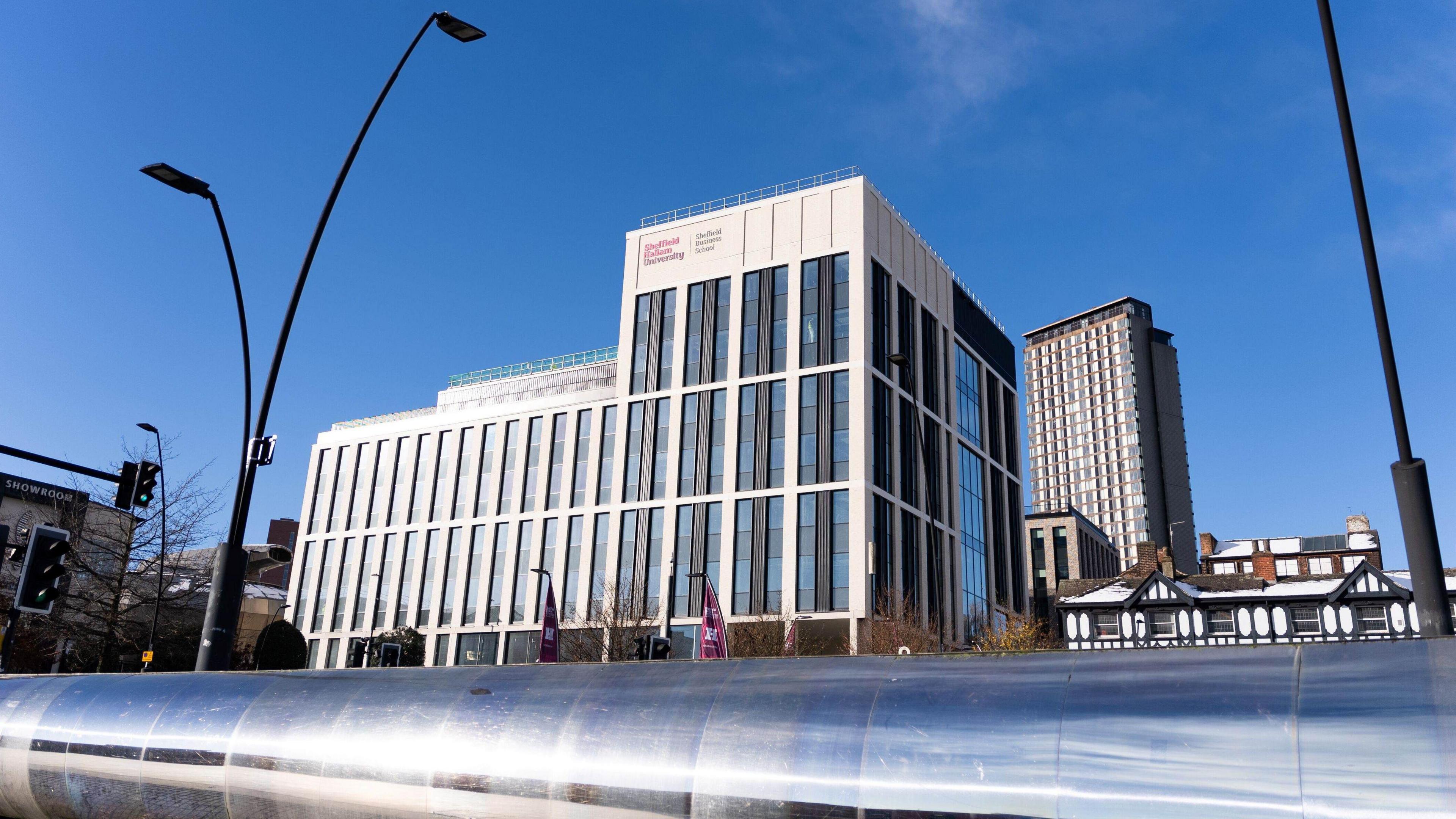 A new building with white walls and glass is in the background, in the foreground is a steel wall